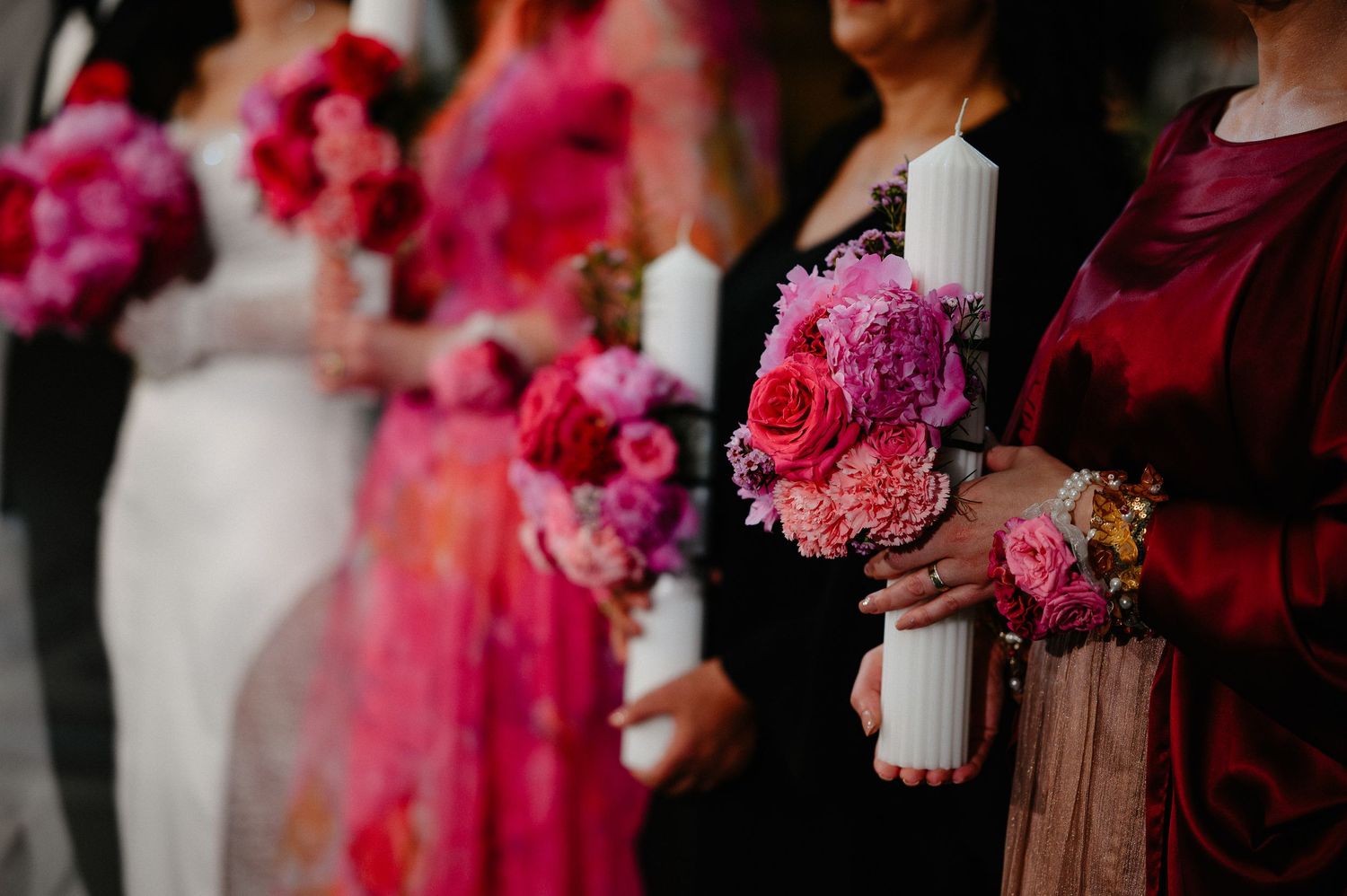 Row of bridesmaids in pink dresses holding matching pink and fuchsia floral bouquets at wedding.