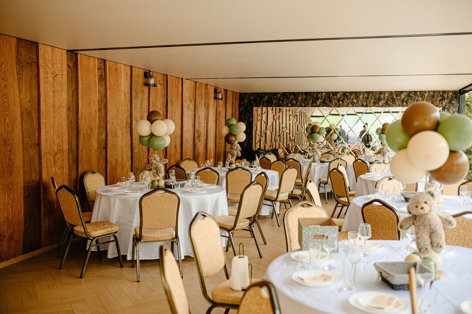 Elegant banquet hall with round tables, balloon centerpieces, and teddy bear decorations.