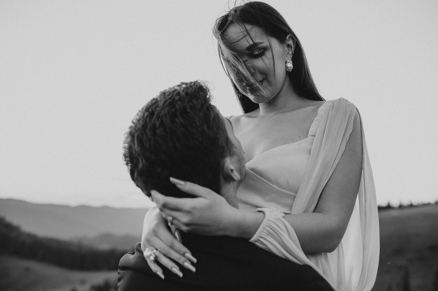 Intimate black and white photo of a bride gazing down at her partner in a romantic outdoor embrace.