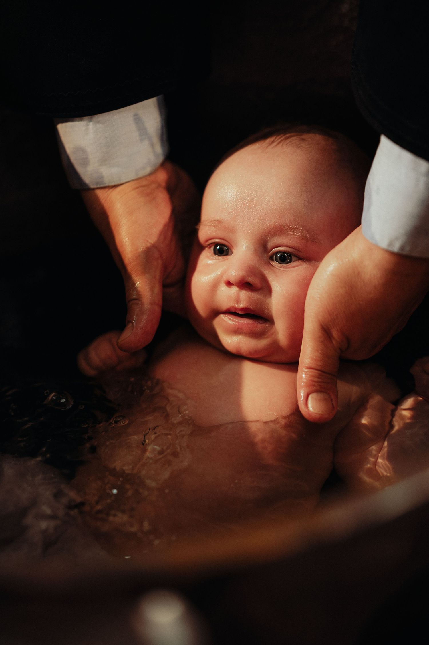 Close-up of a baby being immersed in baptismal water during an Orthodox christening ceremony.