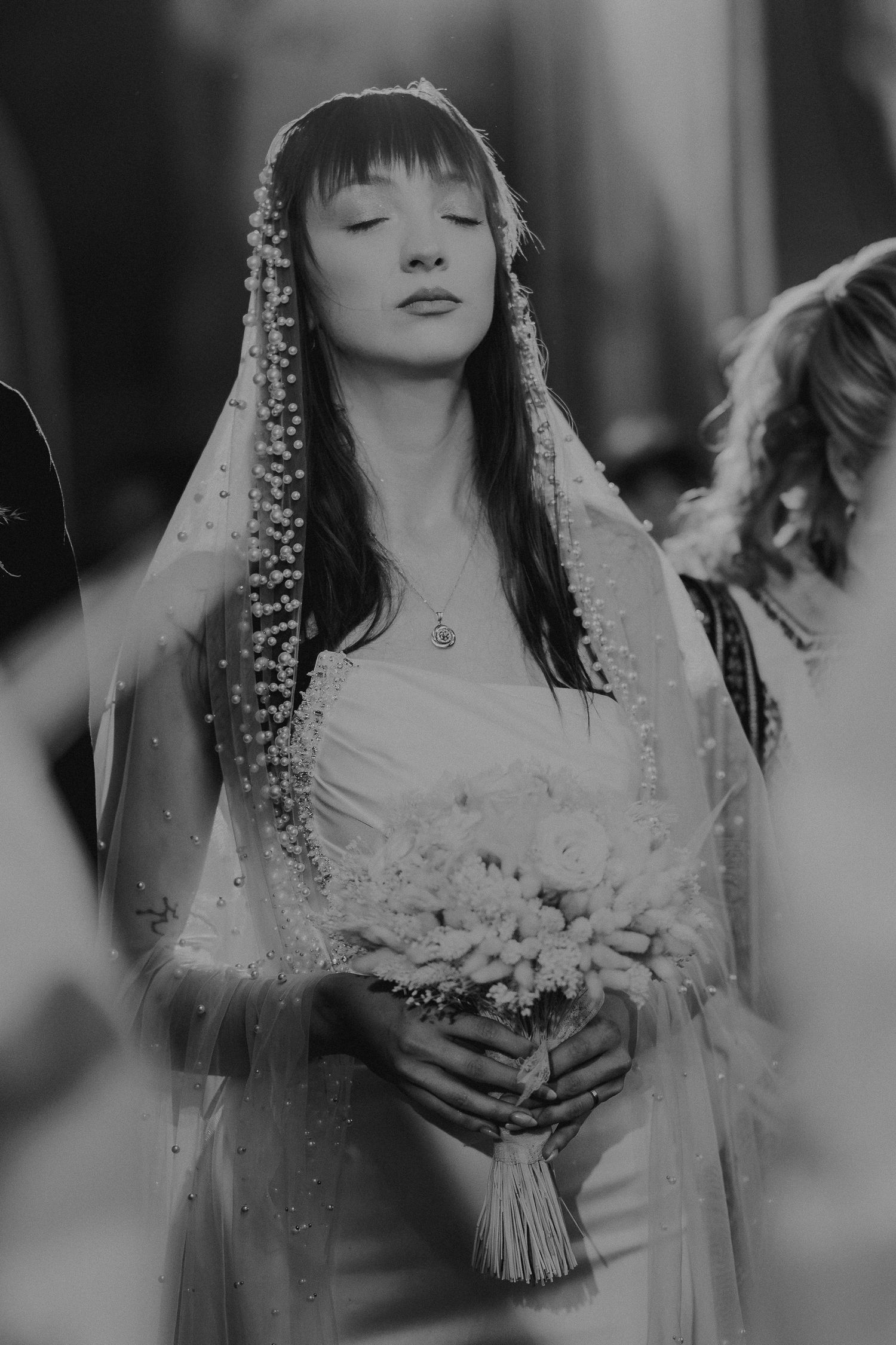 Black and white portrait of serene bride in pearl veil holding bouquet with eyes closed.
