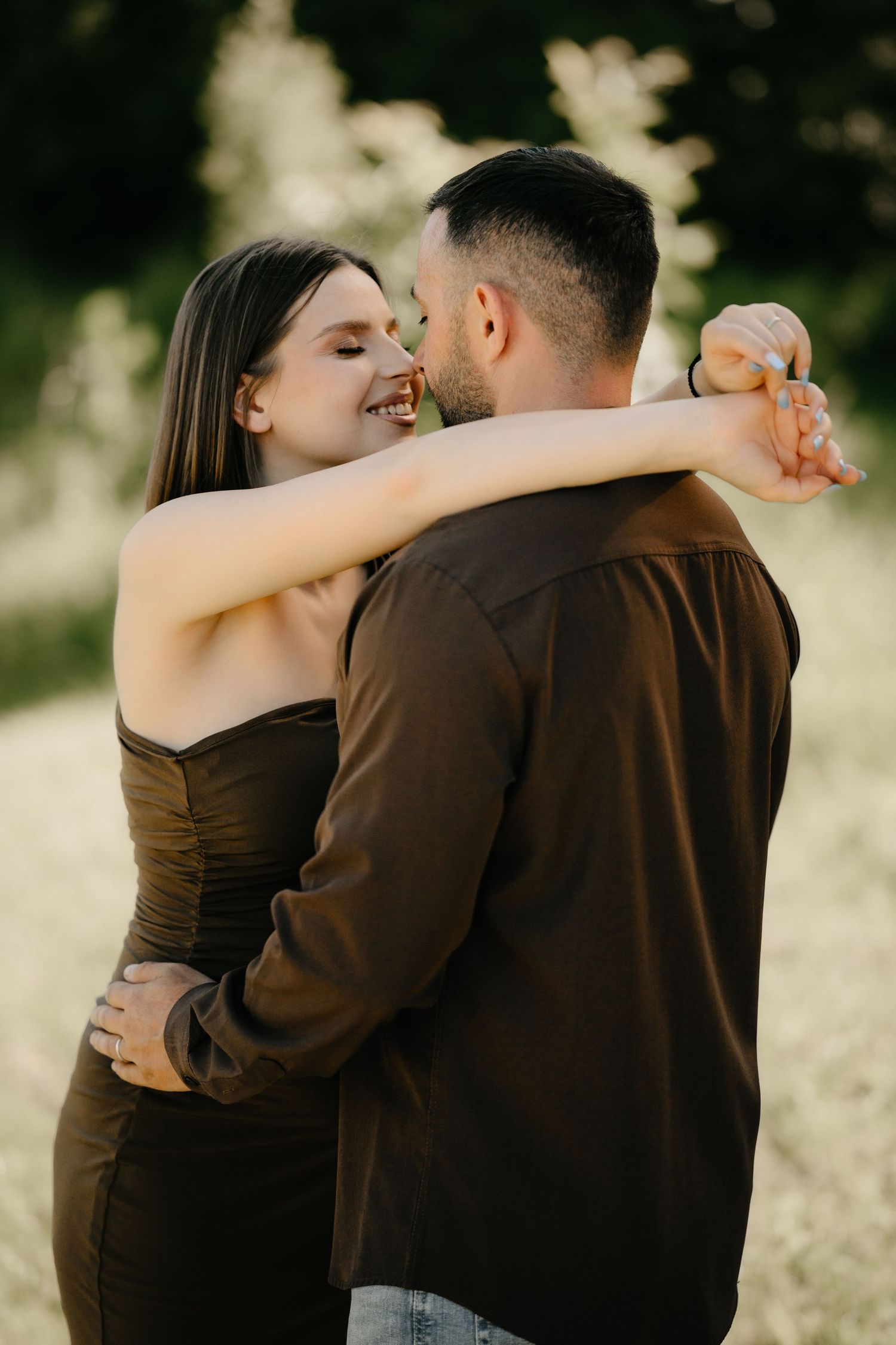 Joyful couple embracing outdoors, woman in dark dress laughing while hugging partner.