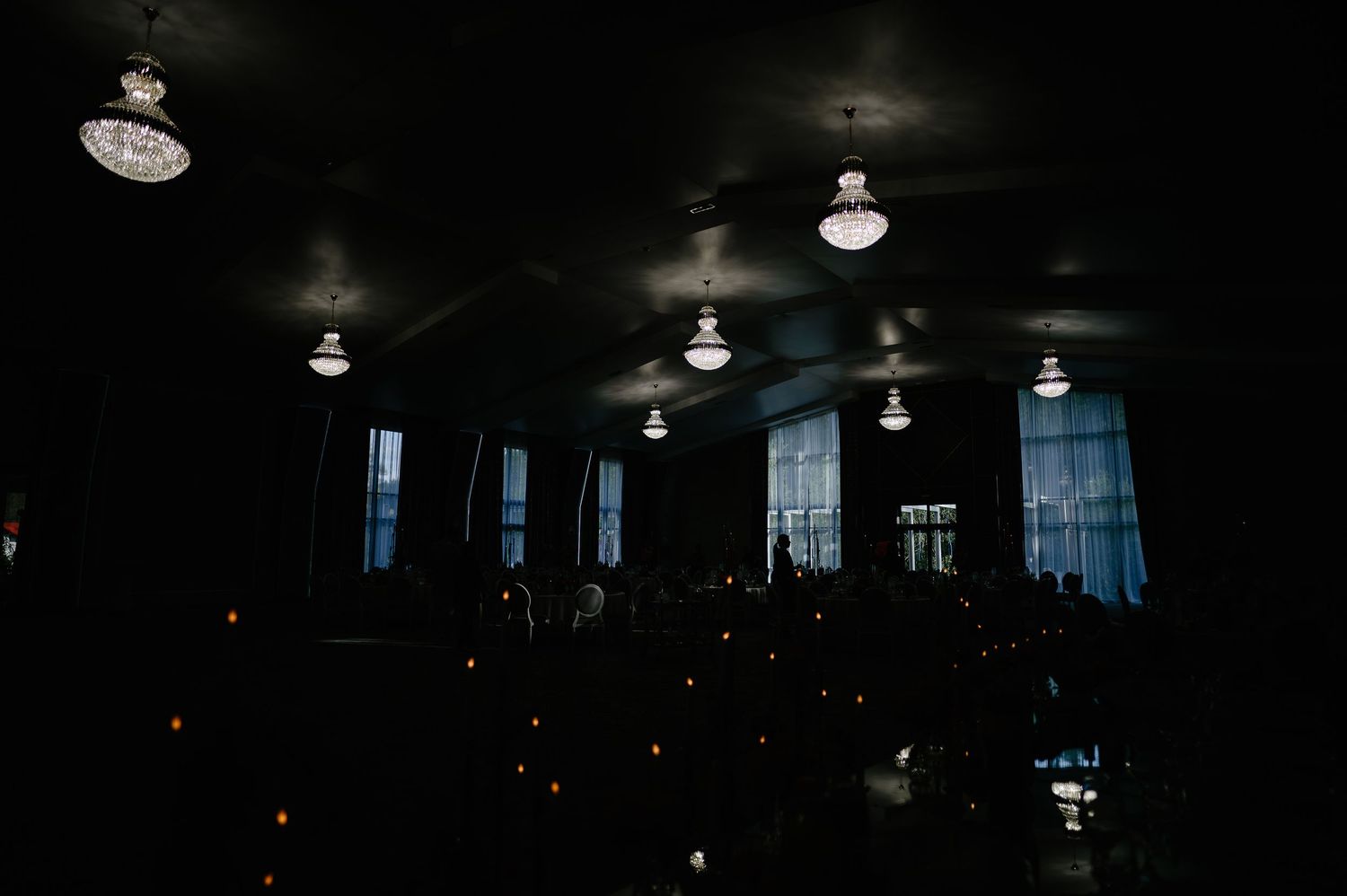 Dark moody wedding reception hall with chandelier lighting and candlelit tables.