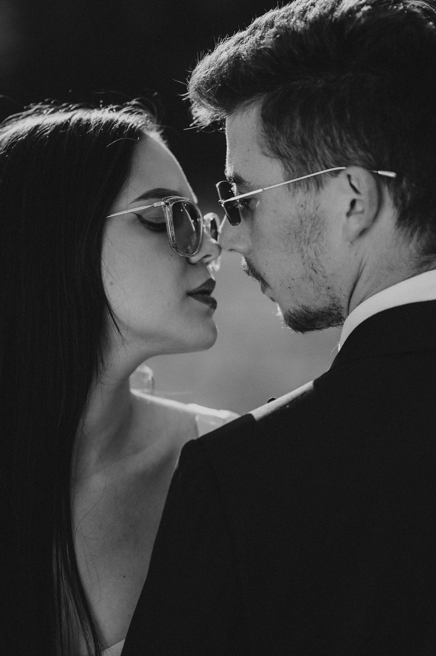 Black and white close-up of couple wearing sunglasses nearly kissing in a romantic portrait.
