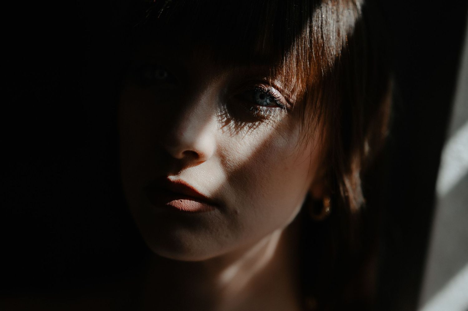 Dramatic moody portrait of a bride with dark hair illuminated by natural light and shadows.