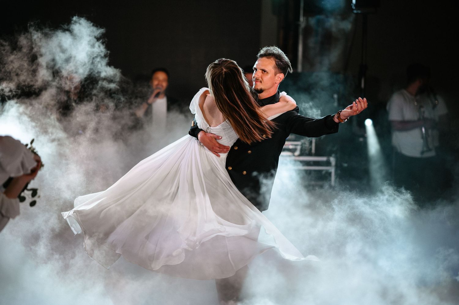 Bride and groom share romantic first dance surrounded by dramatic fog on wedding reception dance floor.