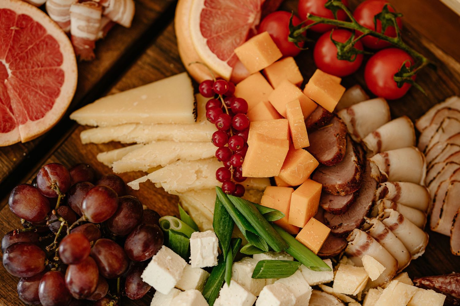 Colorful charcuterie board featuring cheese, grapes, grapefruit, tomatoes, and fresh basil.