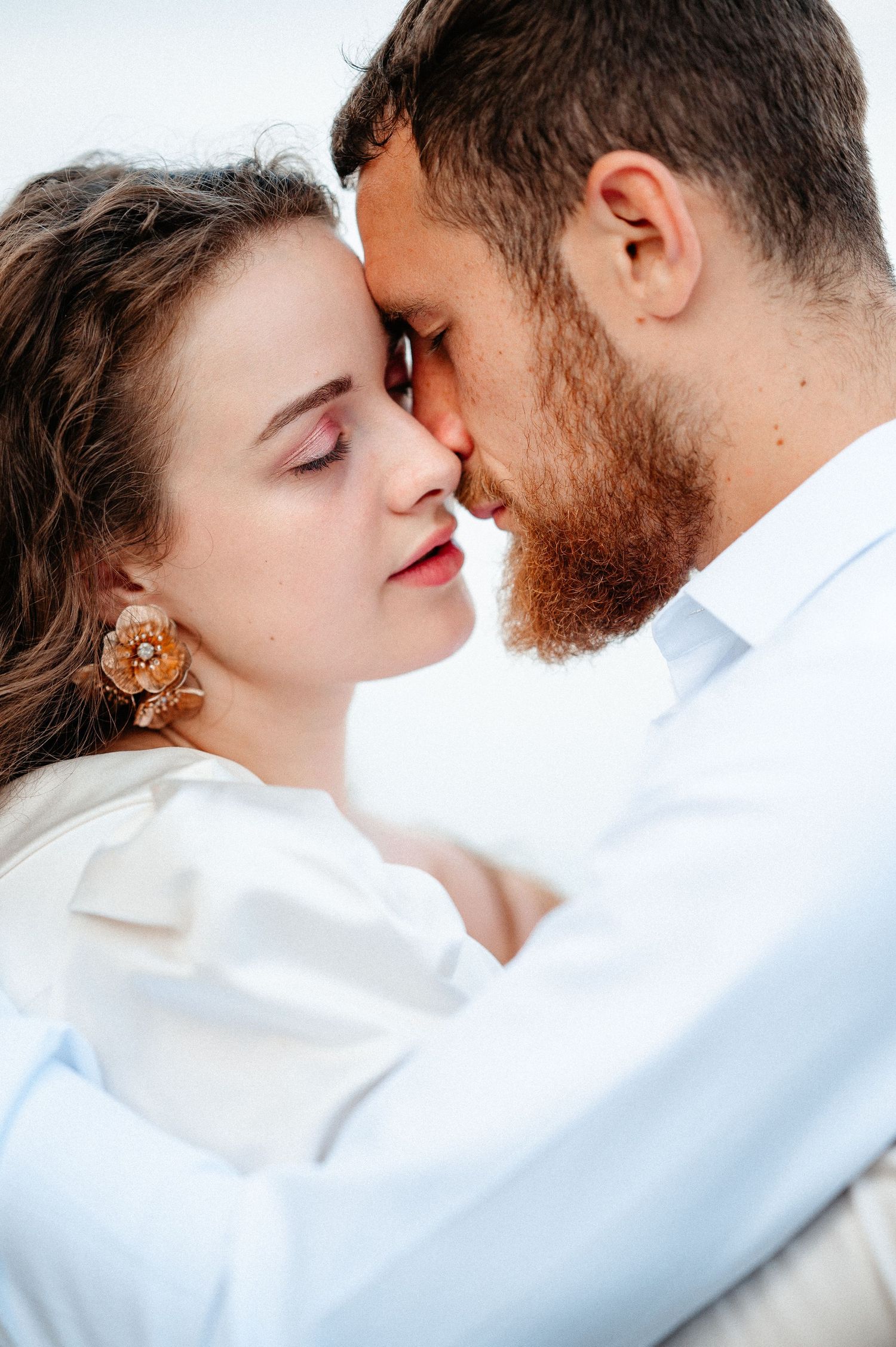 Intimate close-up of couple touching foreheads tenderly, woman wearing floral earrings.