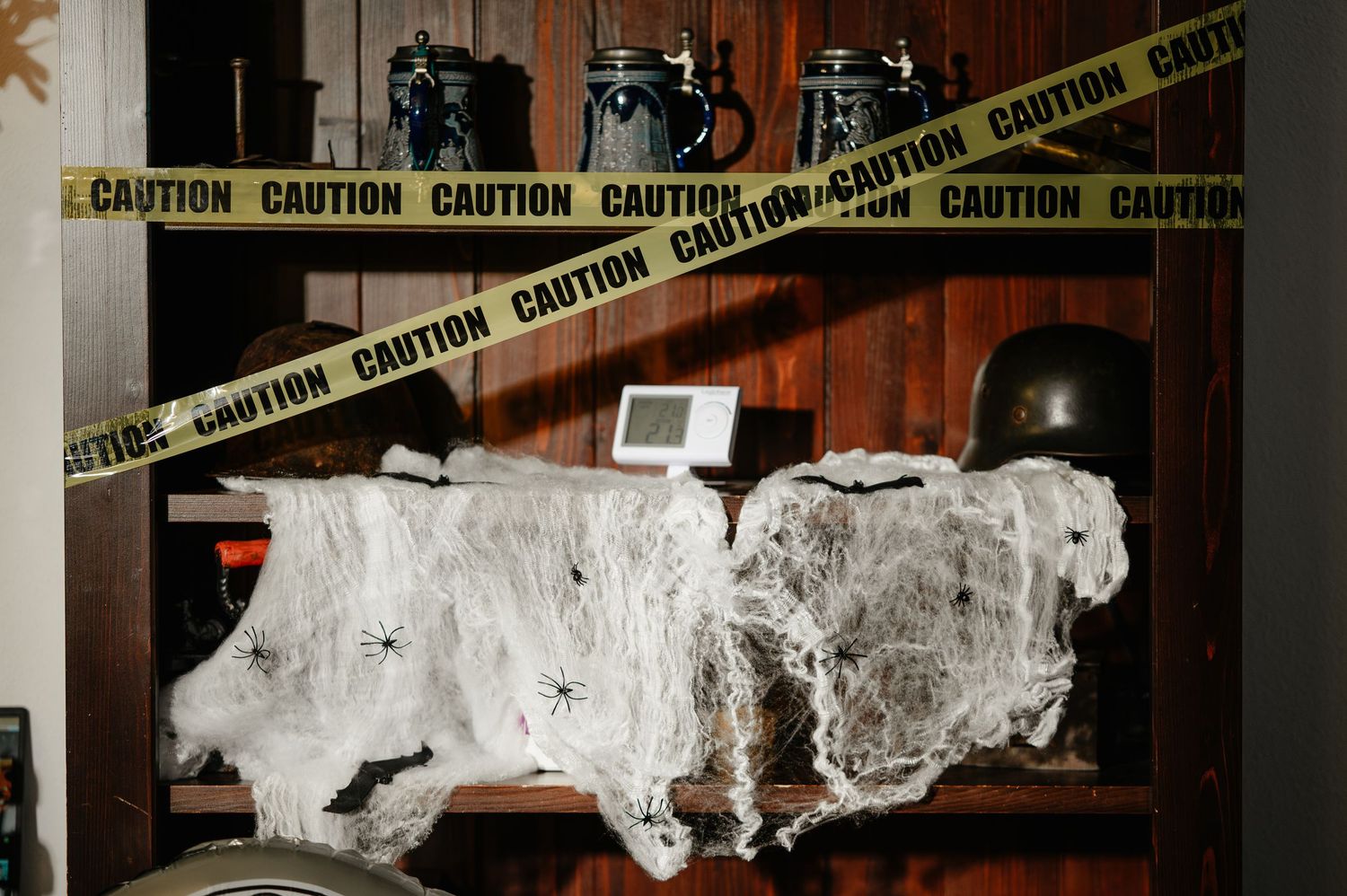 Spooky Halloween shelf decorated with caution tape, fake cobwebs, and spider decorations in a dimly lit room.