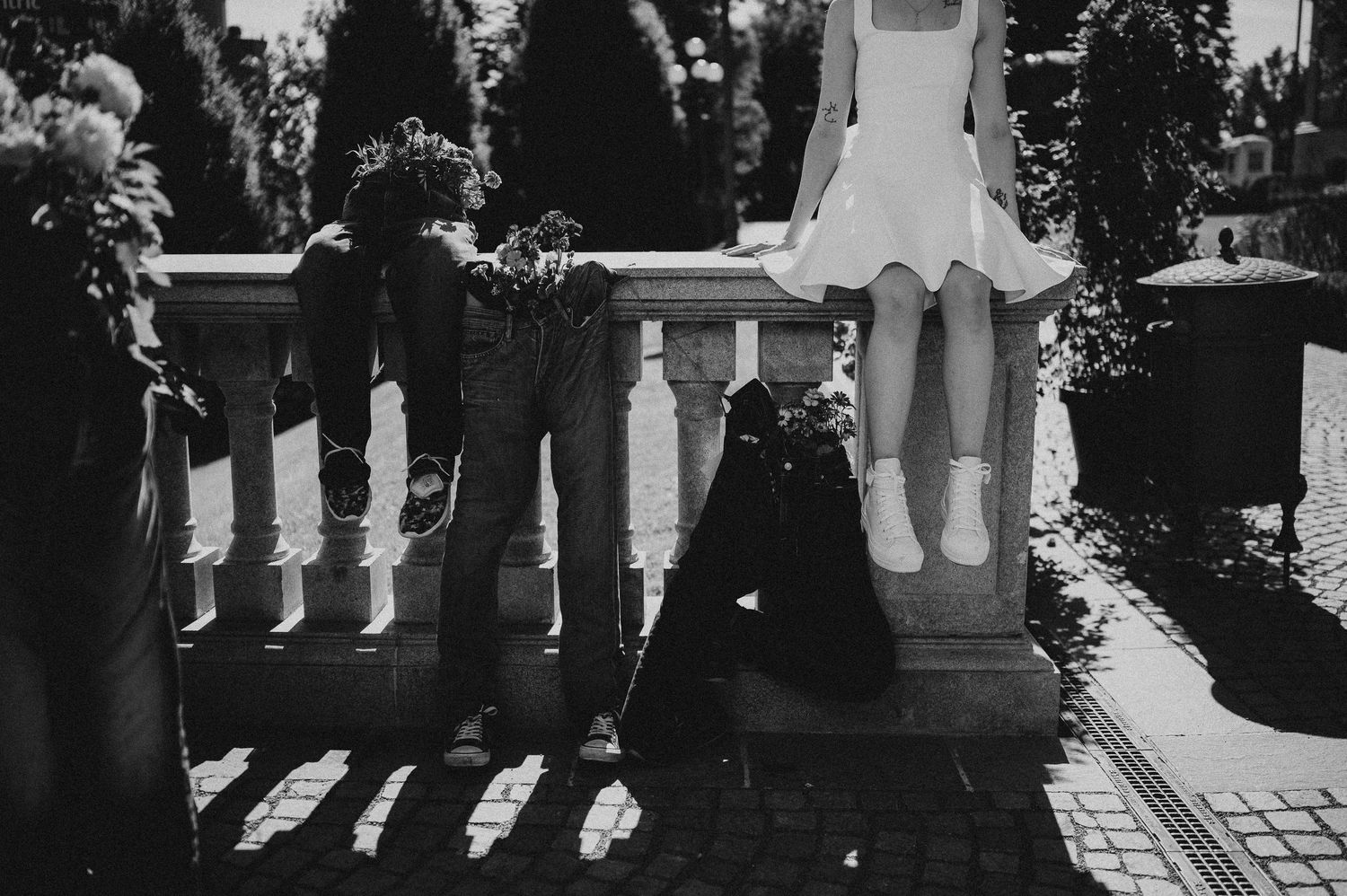 Black and white photo of a couple near a stone balustrade, woman in white dress seated on railing.
