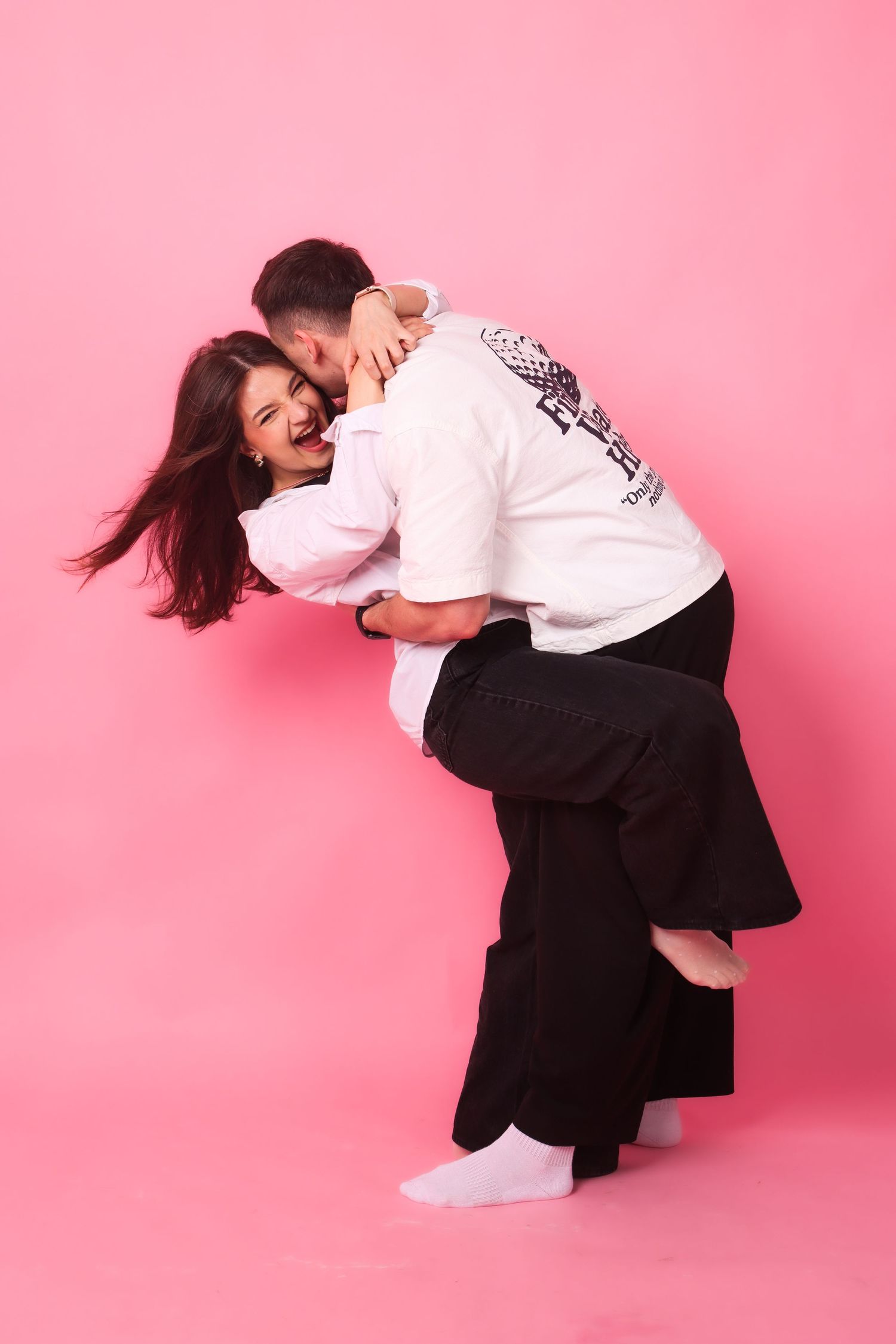 Joyful couple dancing together on a pink studio background, man lifting woman in a playful embrace.