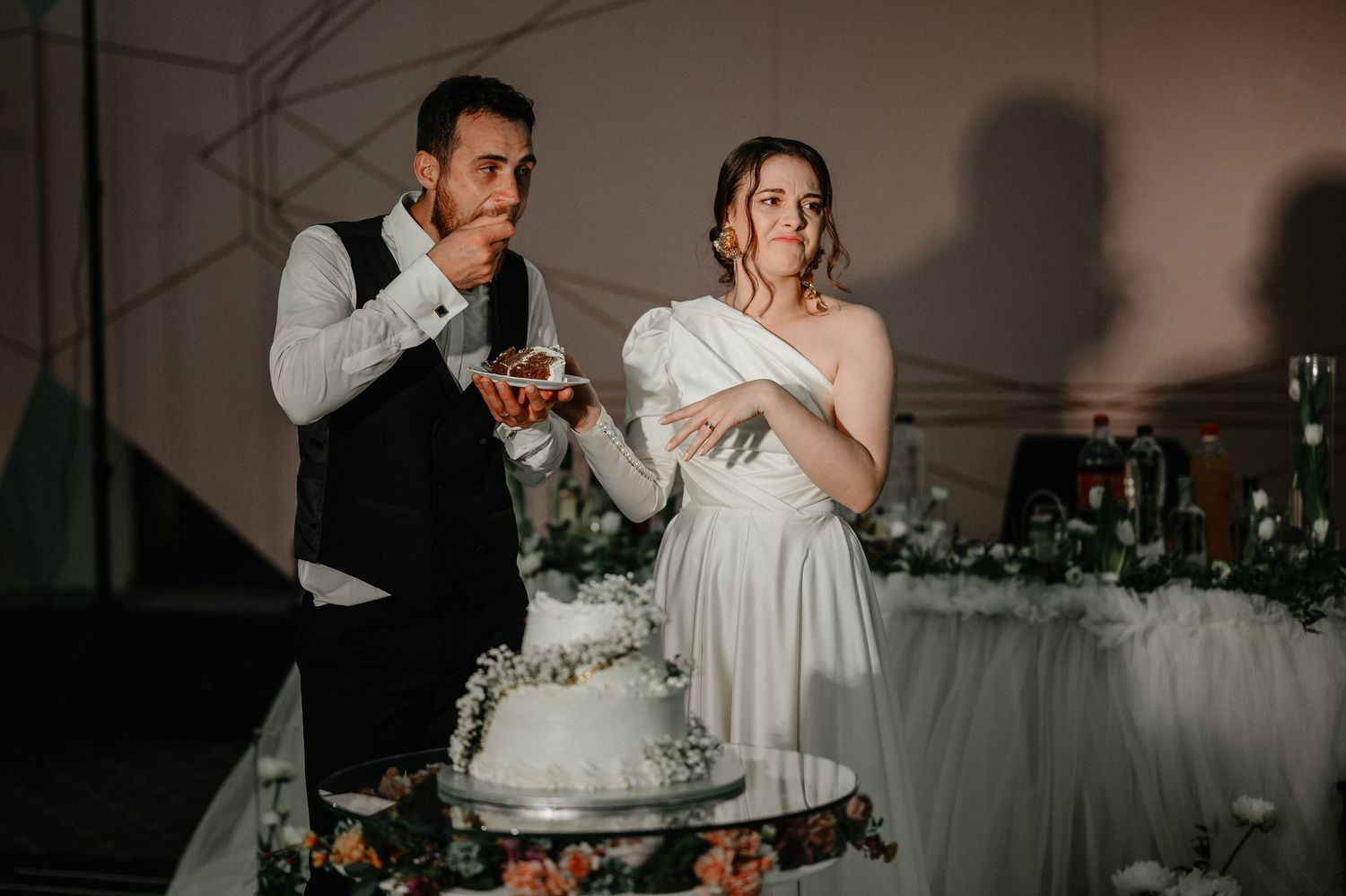 Bride and groom sample wedding cake together at their elegant white and floral decorated reception.