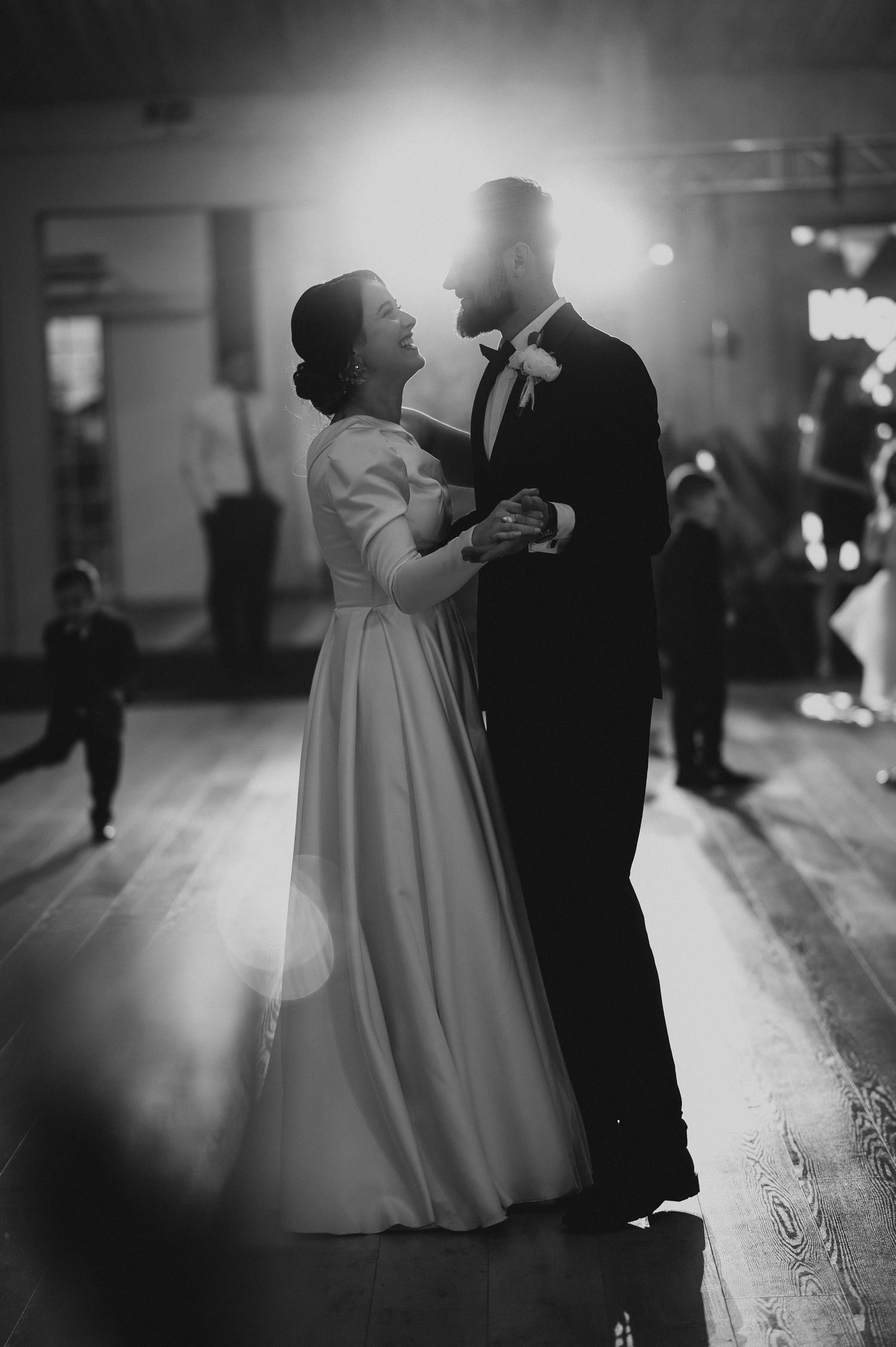Black and white photo of bride and groom sharing first dance under dramatic spotlight at reception.