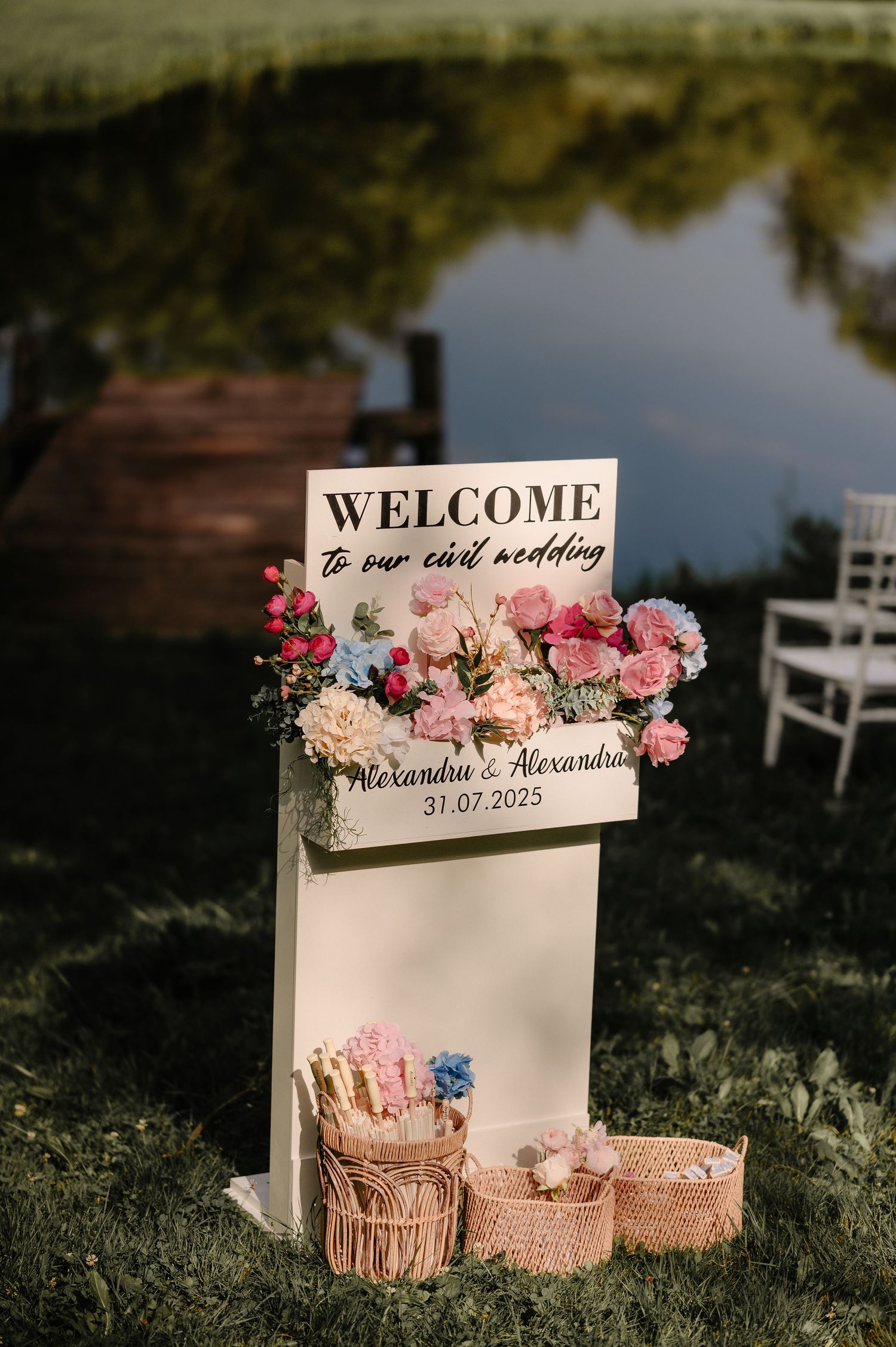 Welcome sign with pink flowers for Alexandru and Alexandra civil wedding on July 31 2023 by a pond.