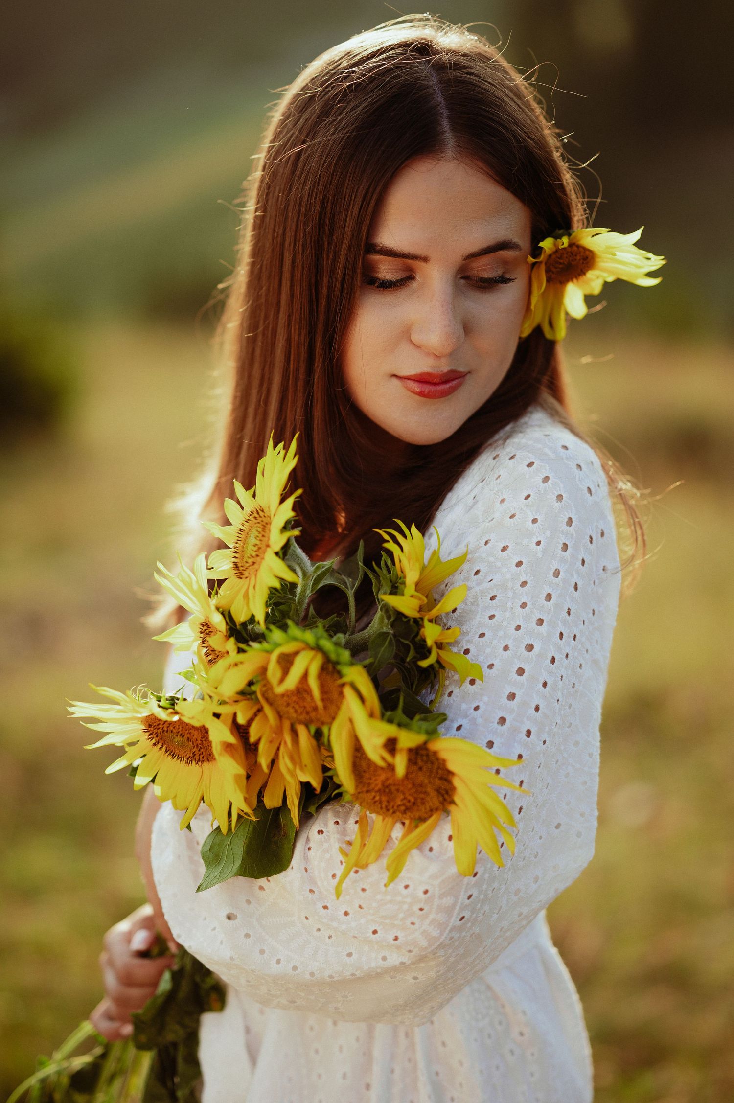 Elegant woman in white eyelet dress gently embracing a bouquet of yellow sunflowers.