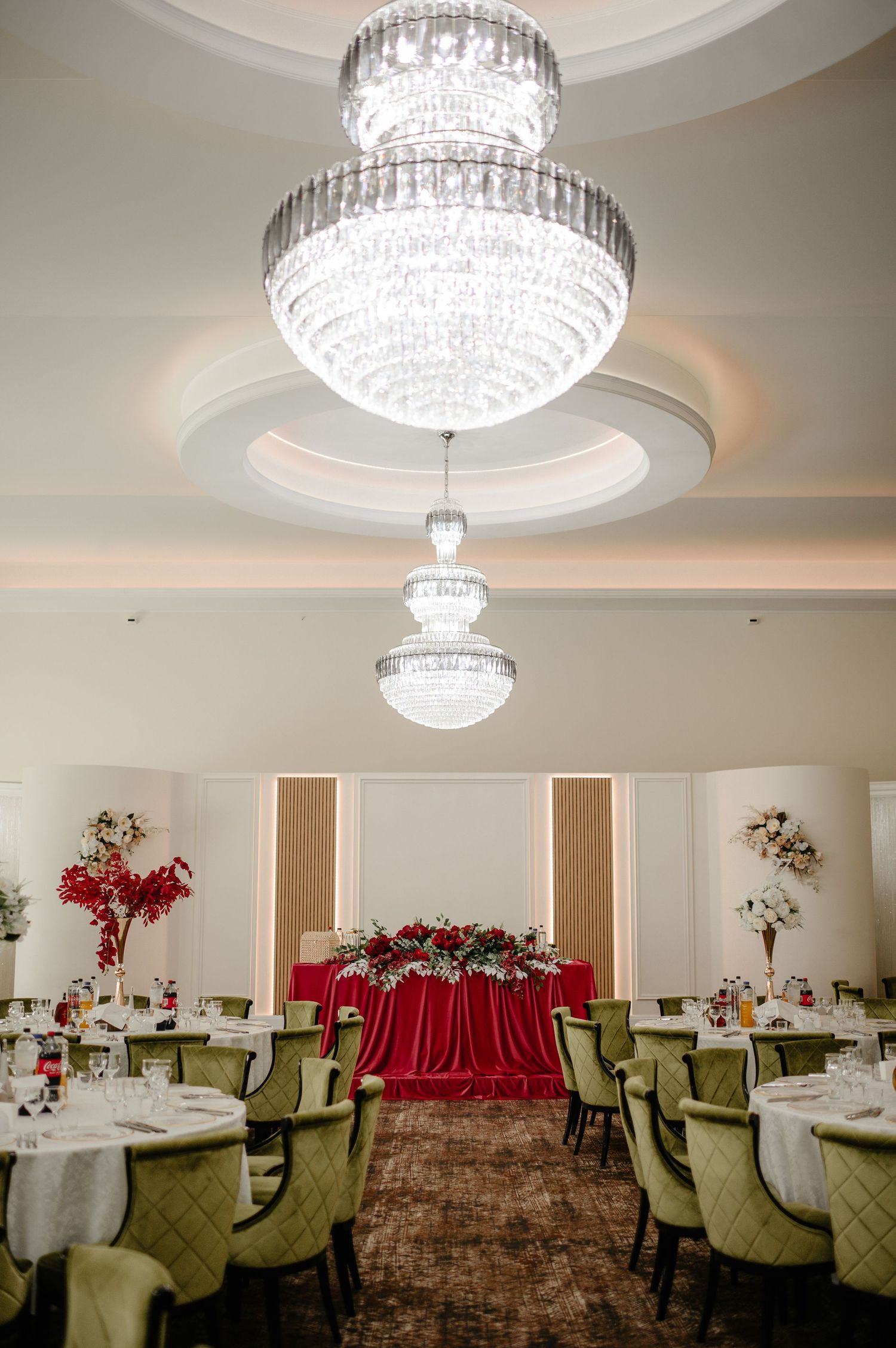 Grand wedding reception ballroom featuring tiered crystal chandeliers and a red-draped sweetheart table.