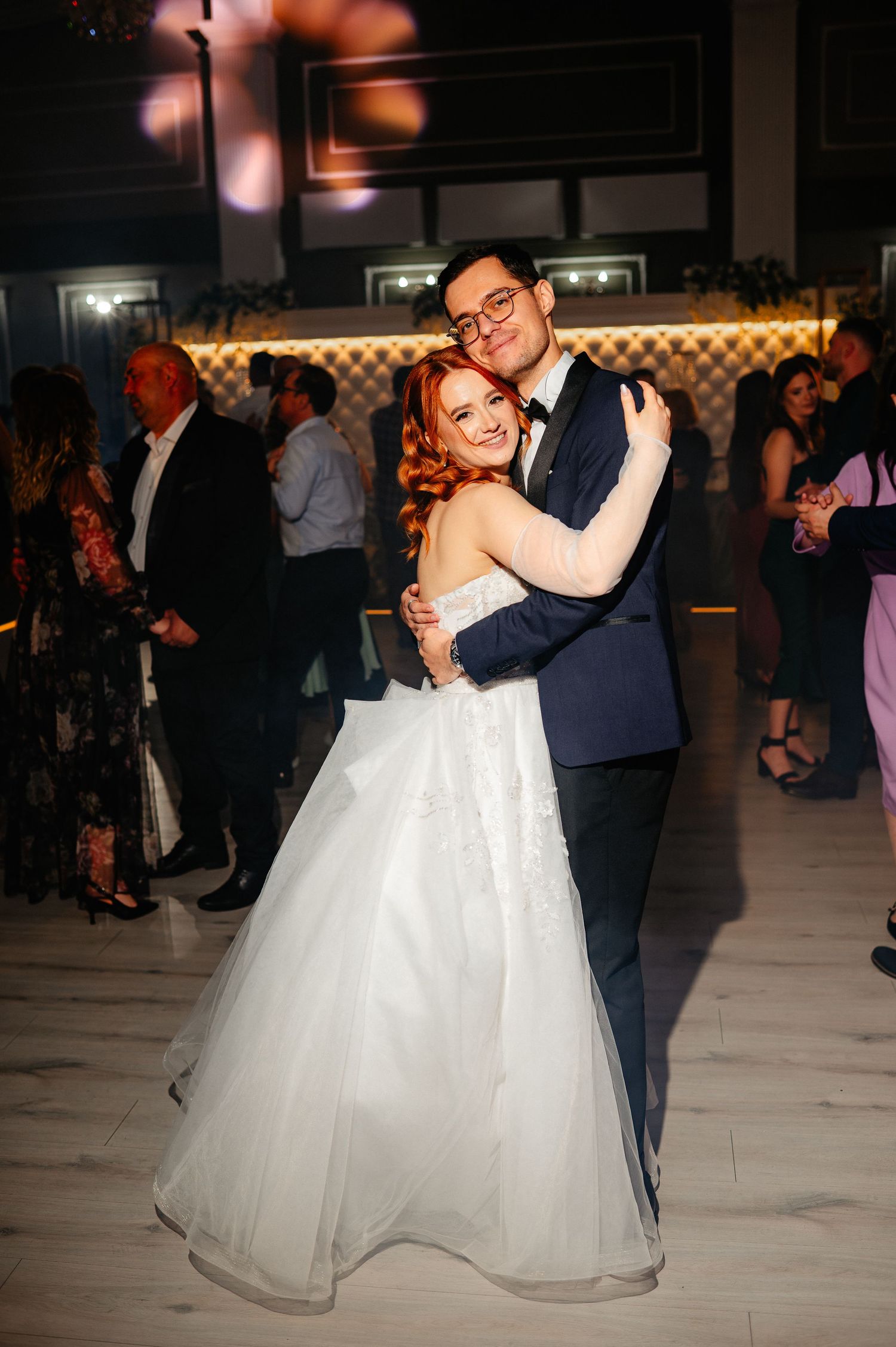 Bride in white ballgown and groom in navy suit share first dance at elegant wedding reception.