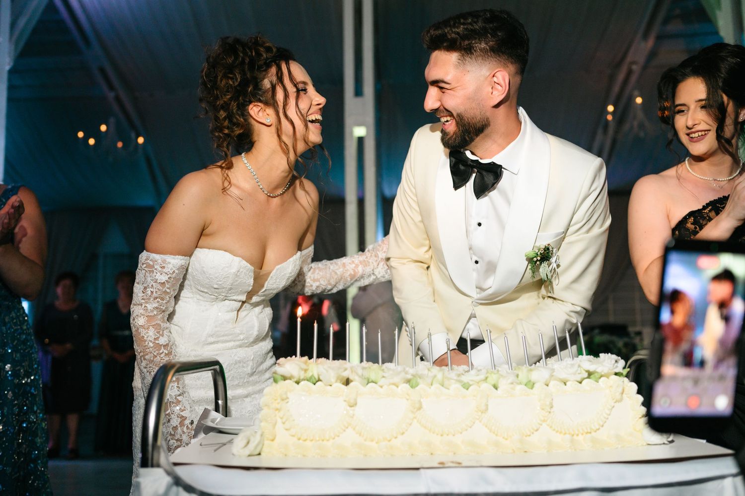 Bride and groom cutting white wedding cake together, smiling at each other during elegant reception celebration.