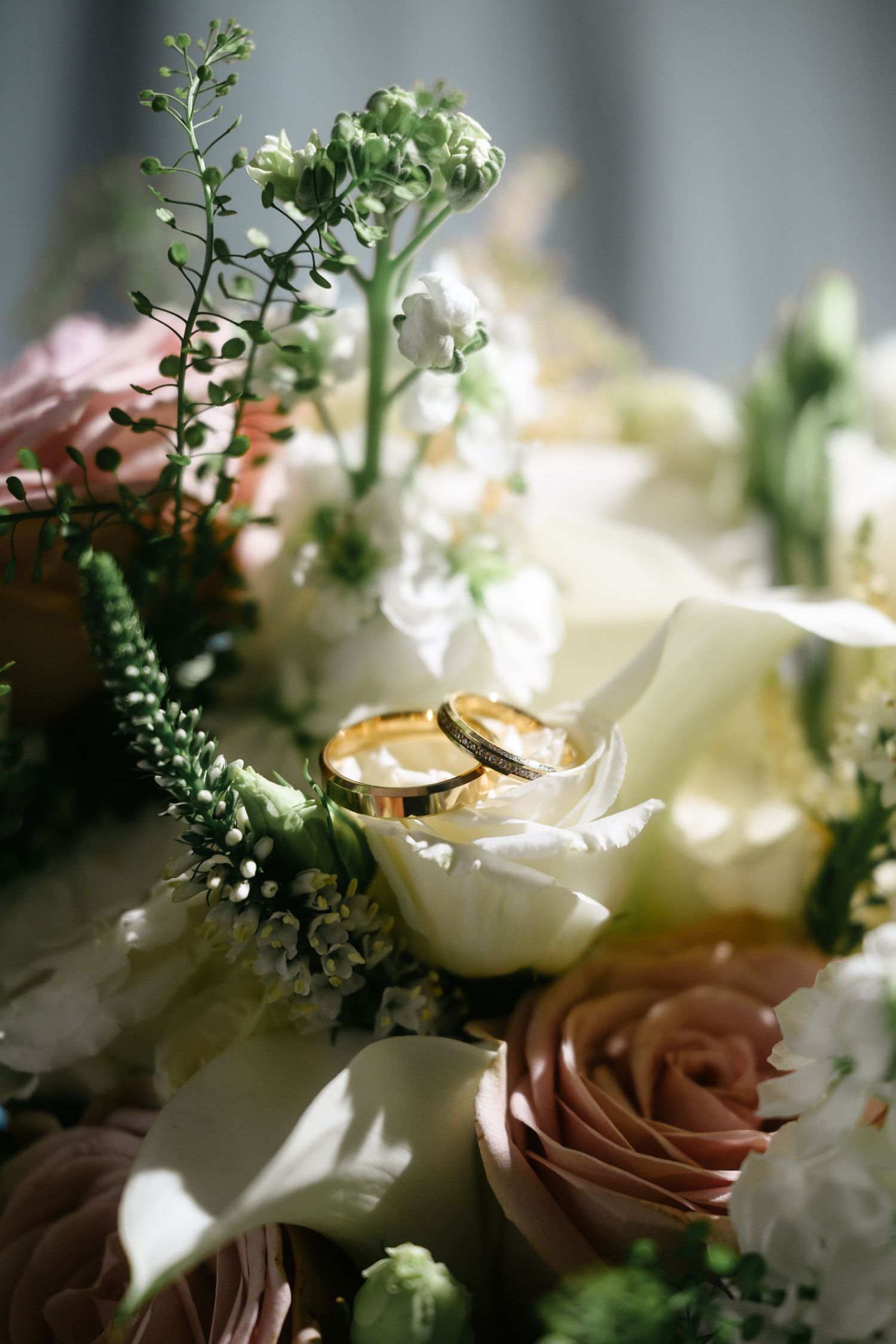 Close-up of two gold wedding bands nestled among white and pink roses in a bridal bouquet.