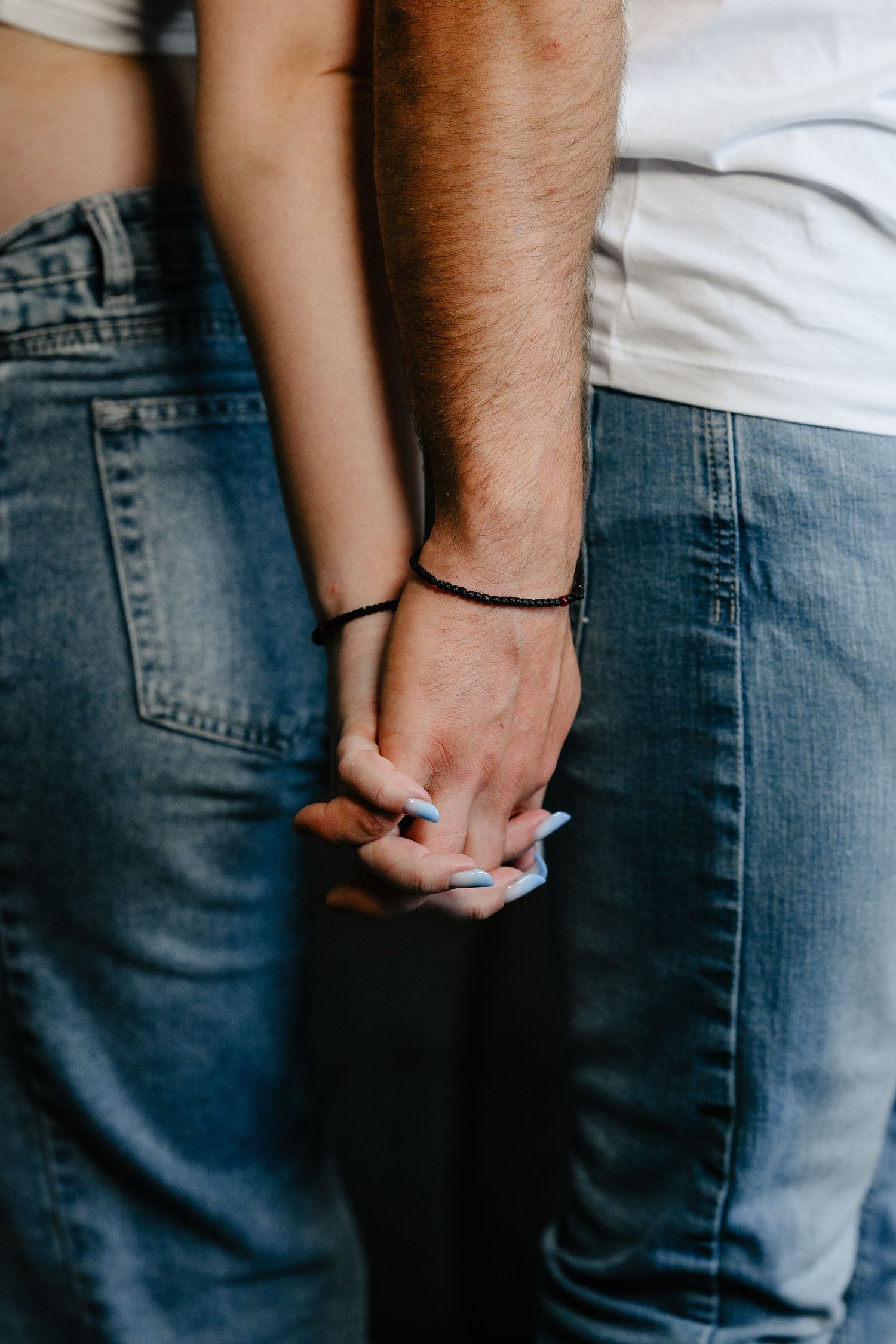 Couple holding hands with matching black bead bracelets, wearing jeans.