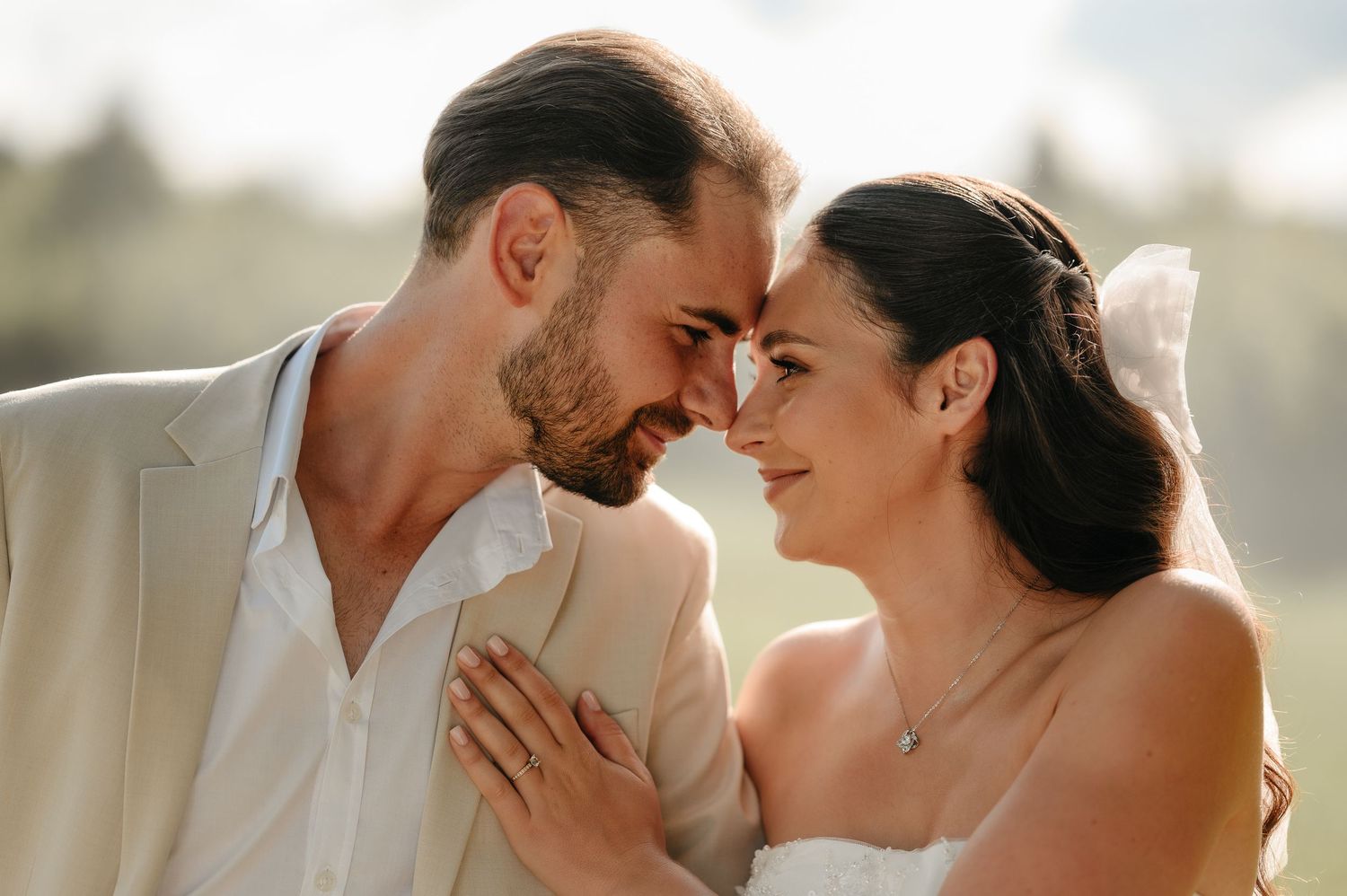 Bride and groom touch foreheads romantically in golden sunlight during outdoor wedding photo session.