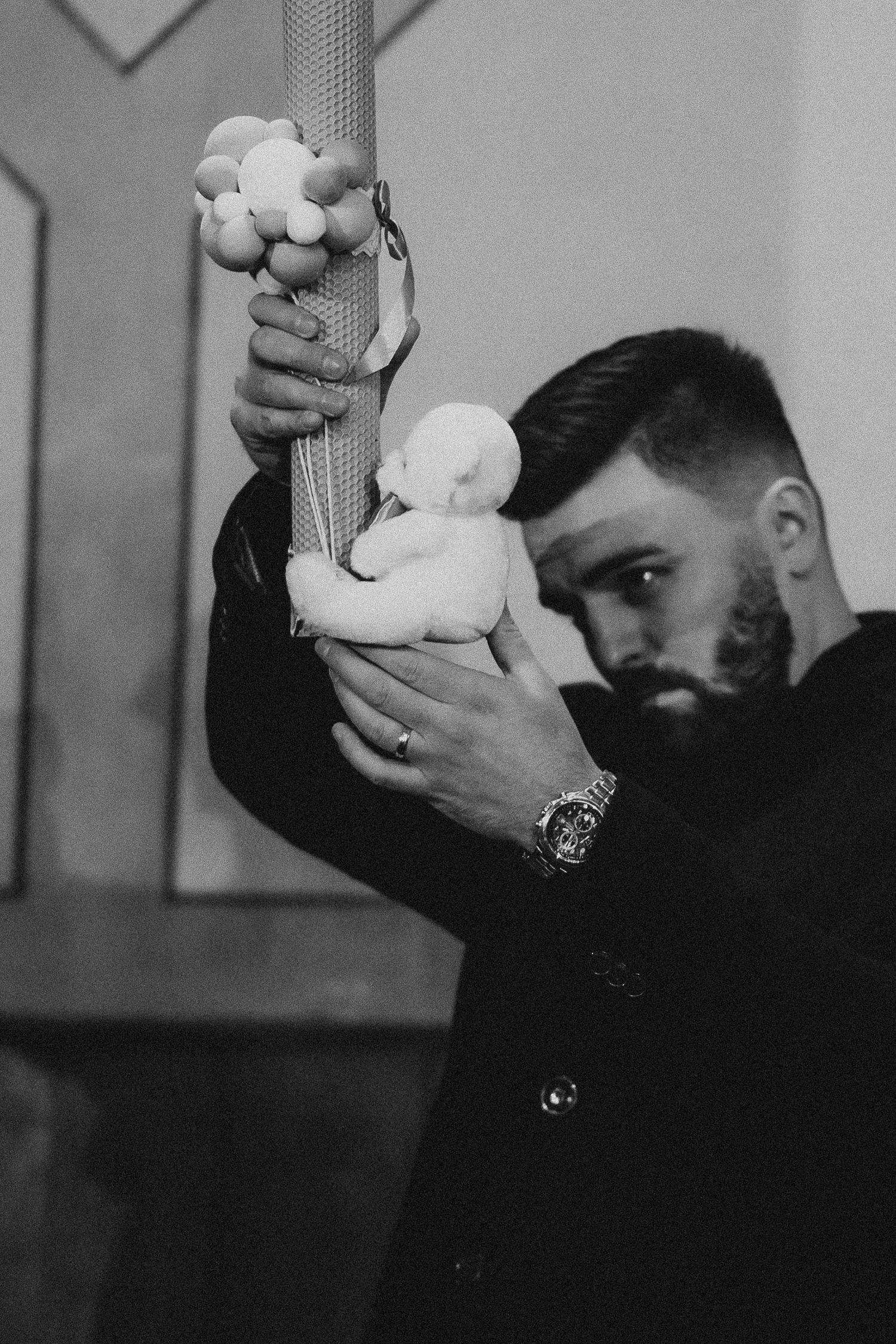Bearded man in black suit holding a decorated baptism candle with white figurine.
