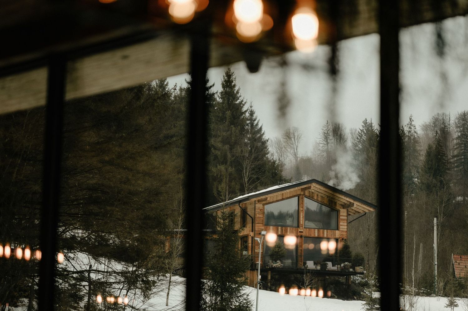 Cozy snow-covered cabin with warm glowing lights viewed through frost-covered window at night.