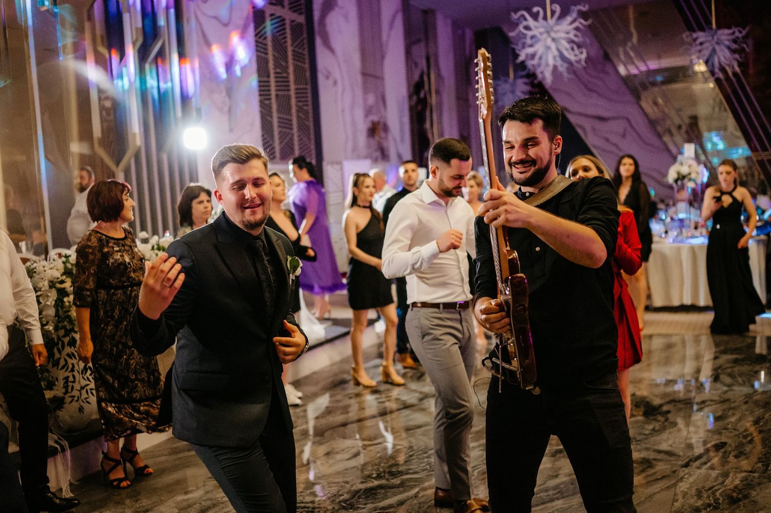 Guests dance and celebrate as a musician plays guitar at a lively wedding reception.