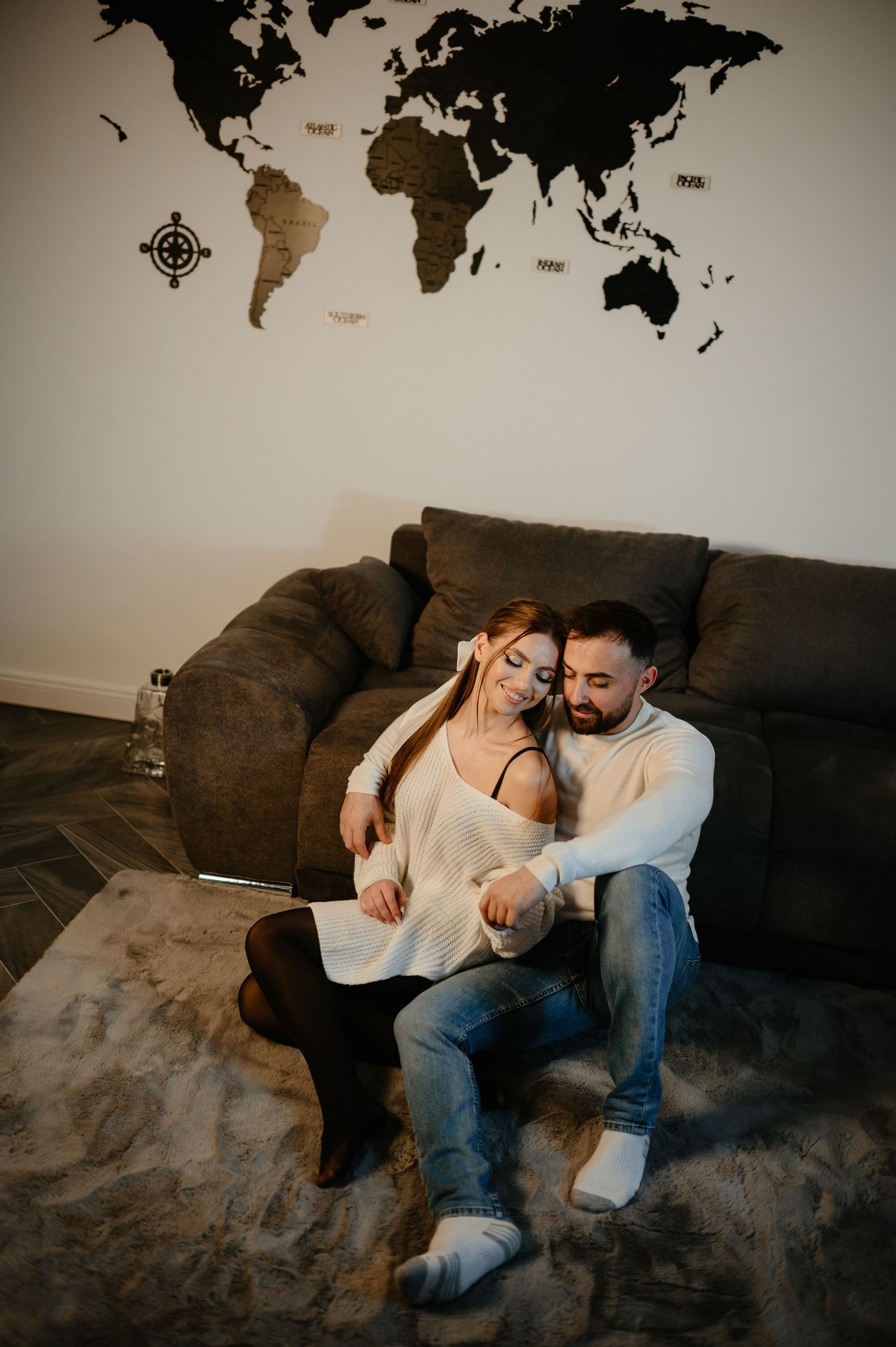 Loving couple sitting together on a couch beneath a world map wall art decoration.
