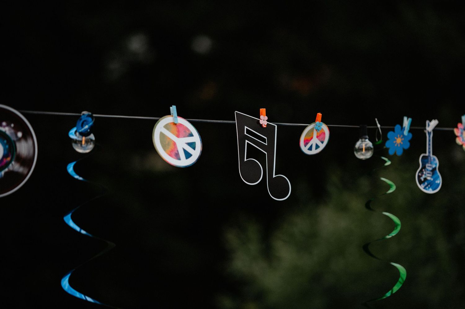 Music-themed party garland with peace signs, musical notes, and guitar decorations against dark background.