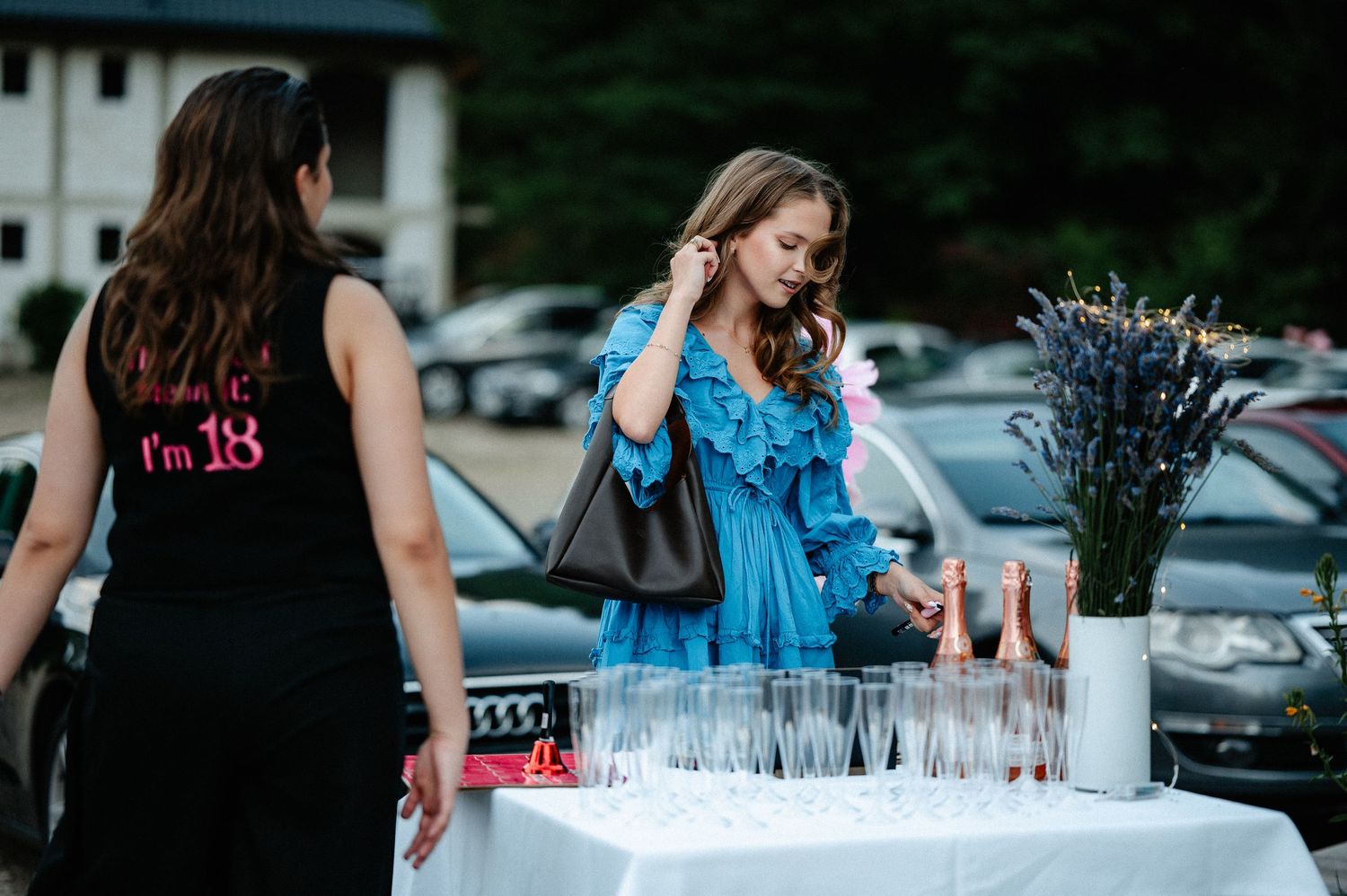 Young woman in blue ruffled dress browsing a drinks table at an outdoor birthday party.