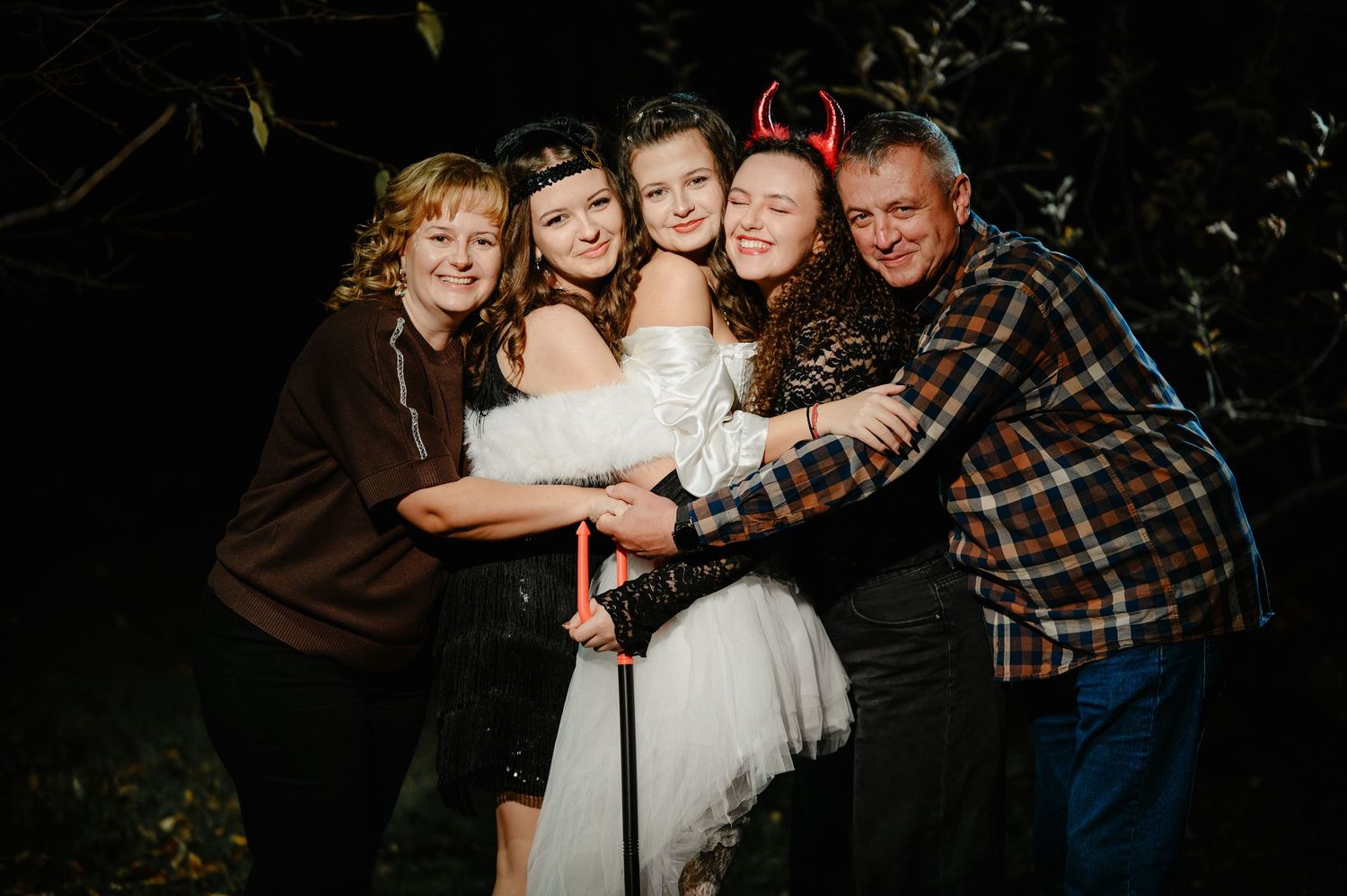 Happy family of five embracing outdoors at night during Halloween celebration in costumes.