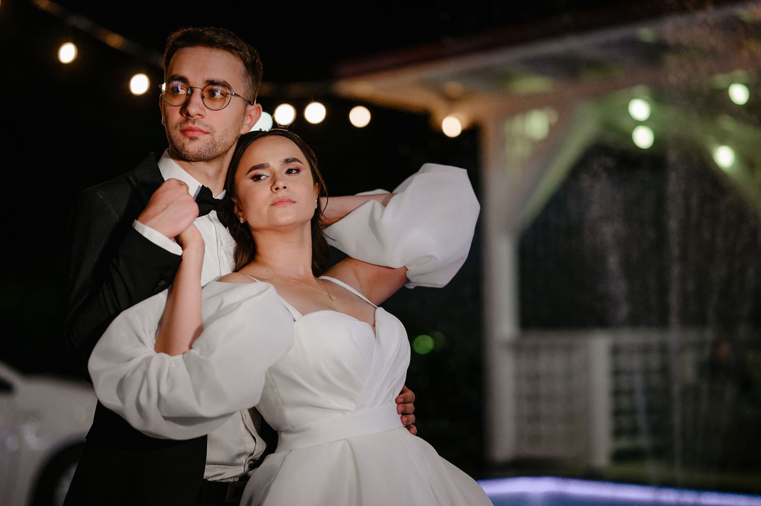 Elegant bride and groom sharing a romantic dance outdoors at night under warm string lights.