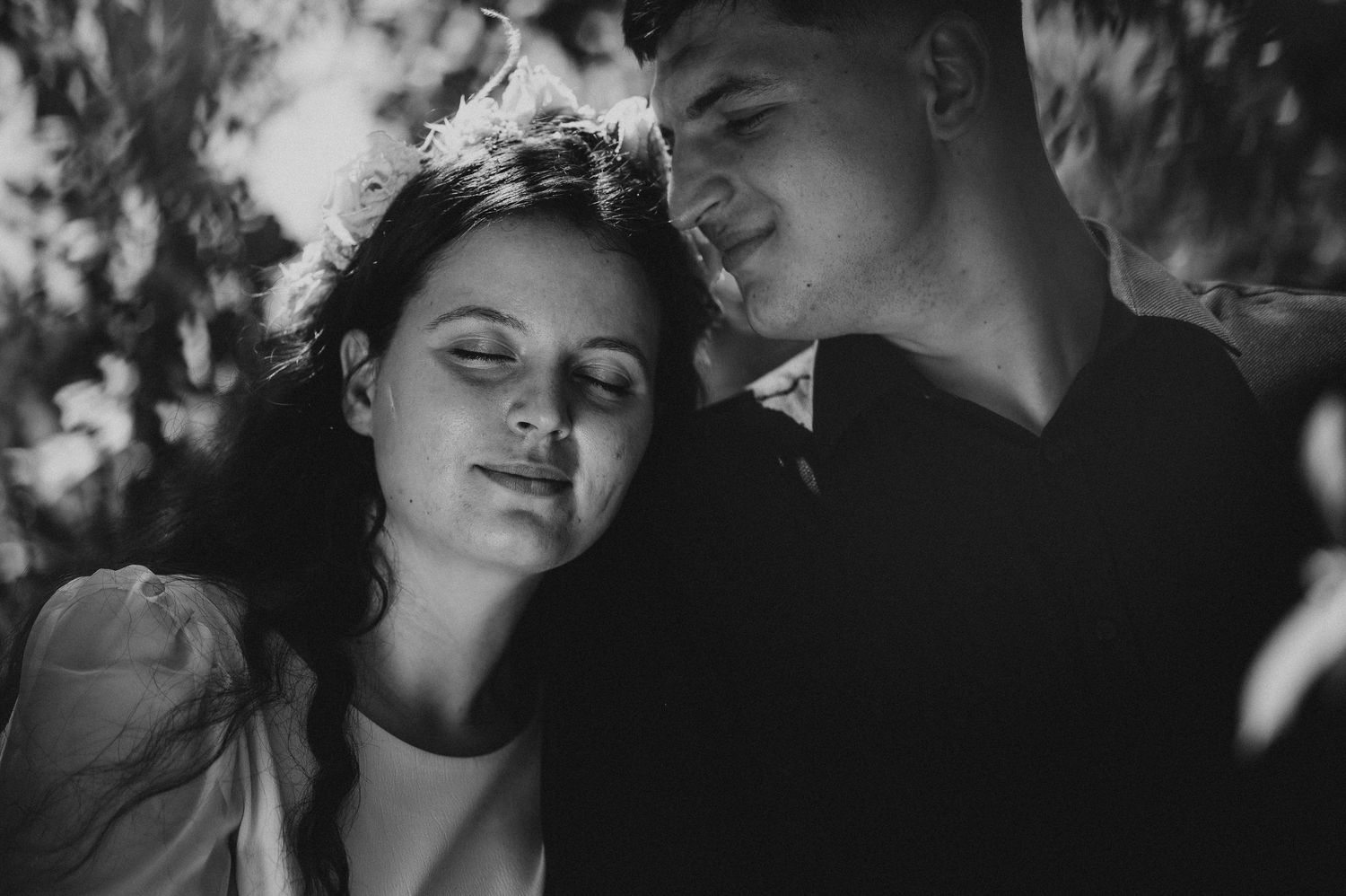 Black and white romantic couple portrait with woman resting head on mans shoulder outdoors.