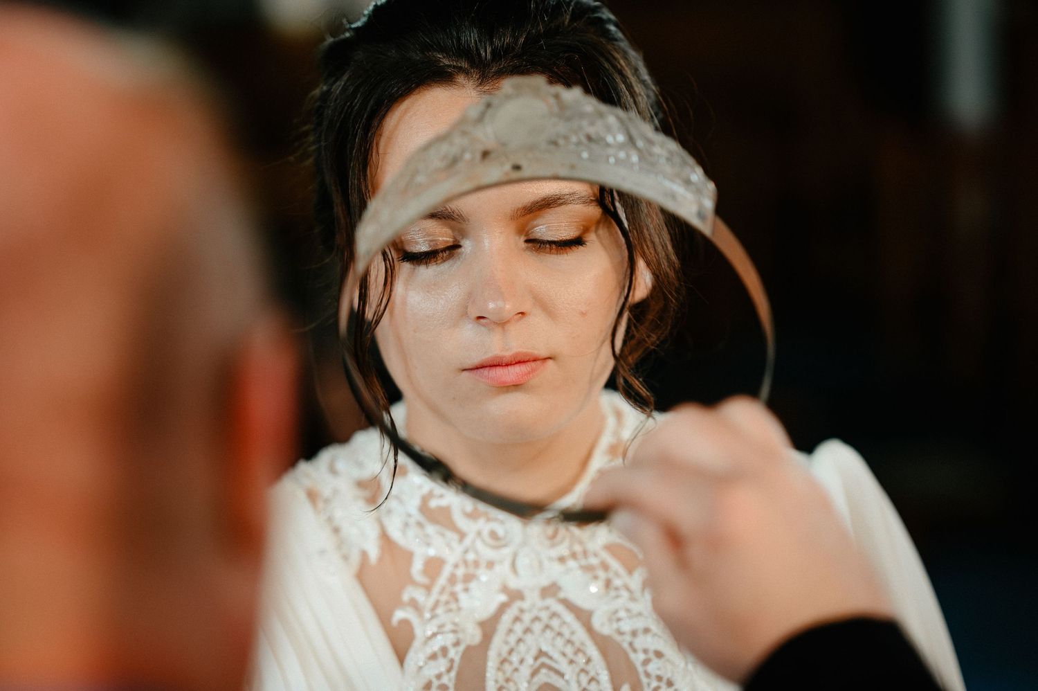 Bride wearing a lace wedding dress and beaded headband with eyes closed during ceremony.