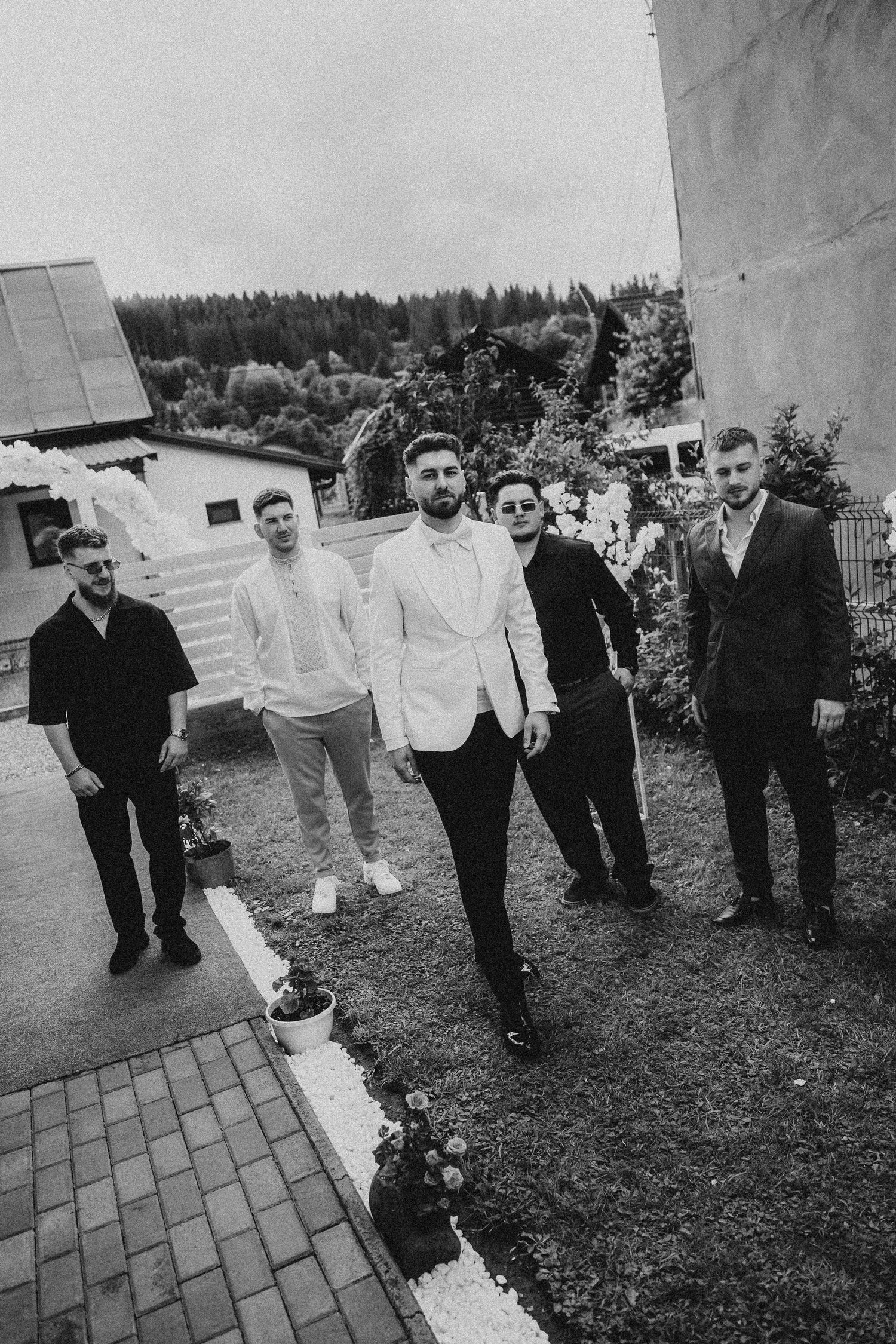 Black and white photo of five well-dressed men posing outdoors near a garden at a formal event.