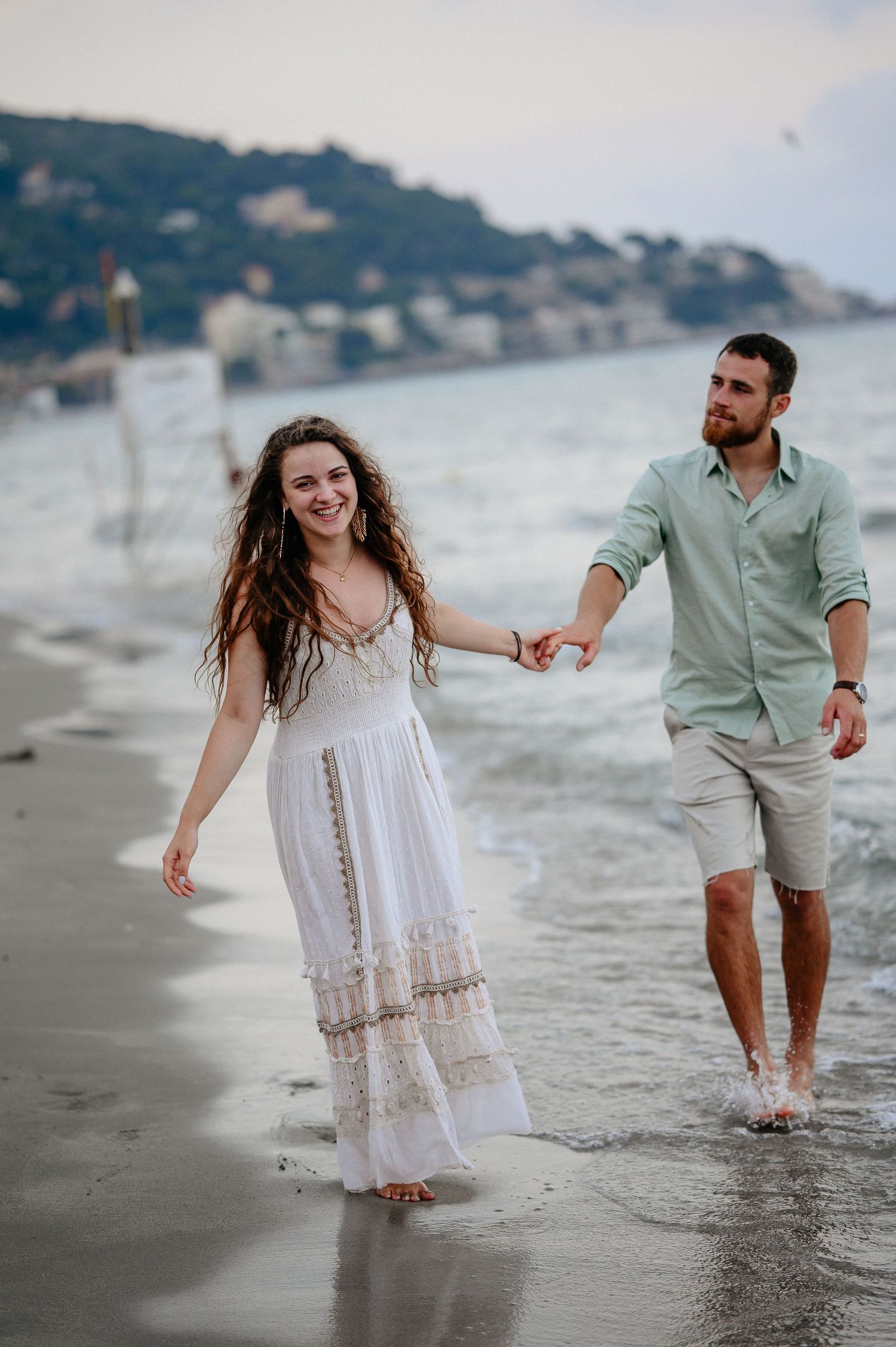 Happy couple holding hands and walking barefoot along a scenic coastal beach.
