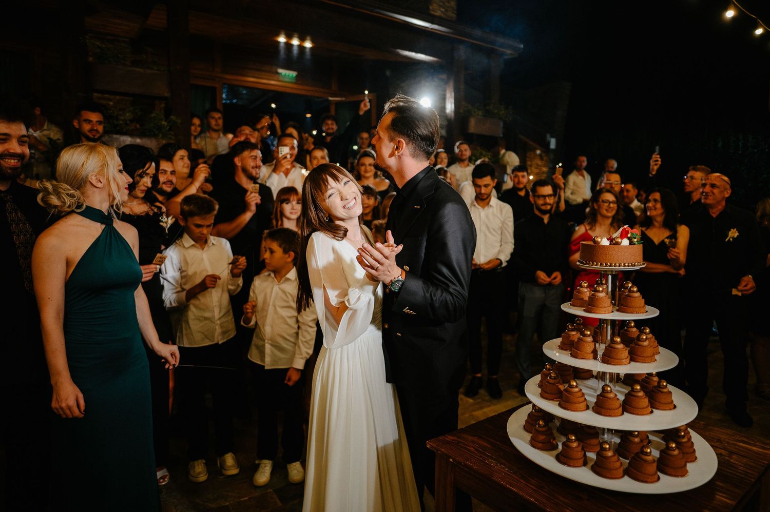 Bride and groom celebrate cake cutting ceremony with joyful guests at elegant wedding reception.