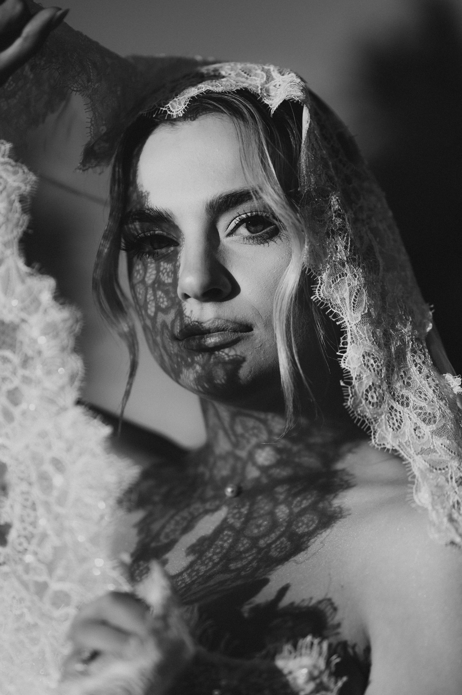 Black and white portrait of a bride wearing lace veil, dramatic lighting highlighting elegant makeup and delicate details.