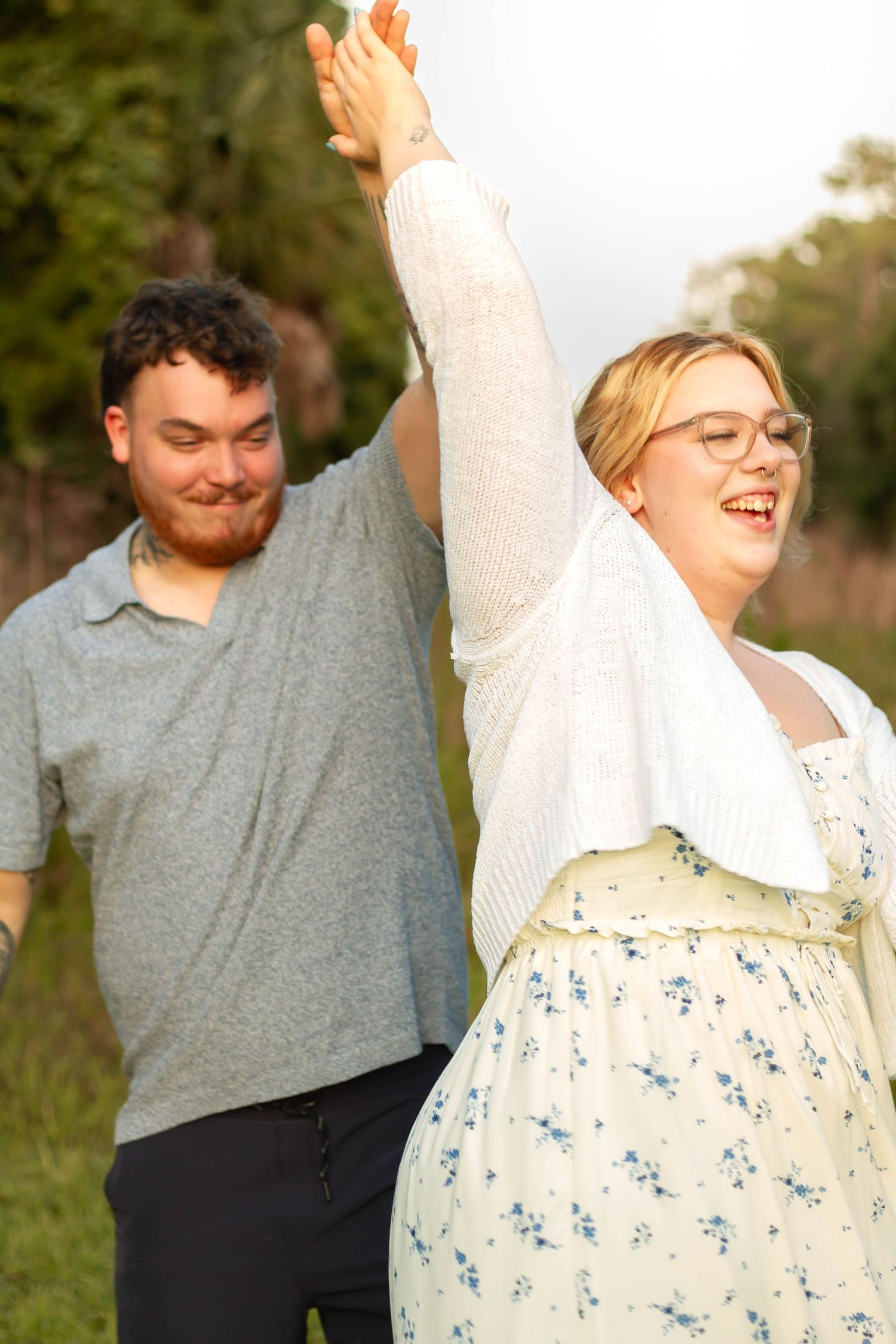 A joyful couple dancing outdoors in golden hour light, woman in floral dress raising their joined hands.