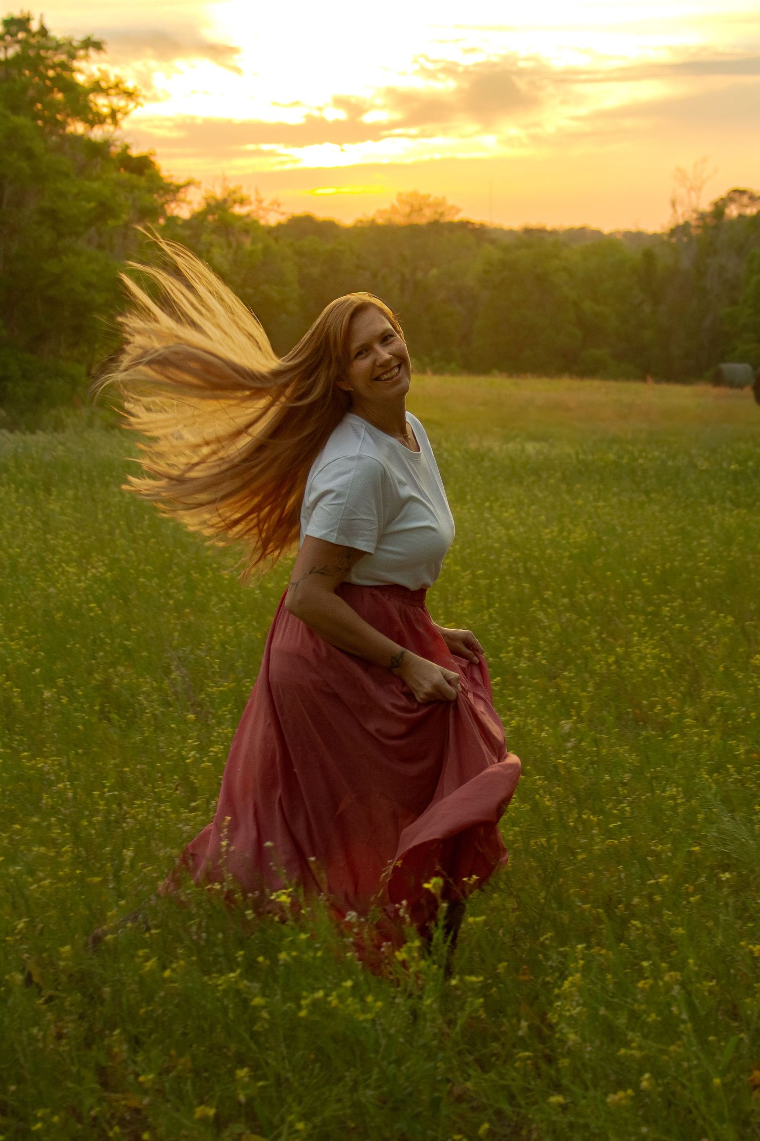 Joyful redhead woman spinning in pink skirt in wildflower meadow during vibrant golden sunset.