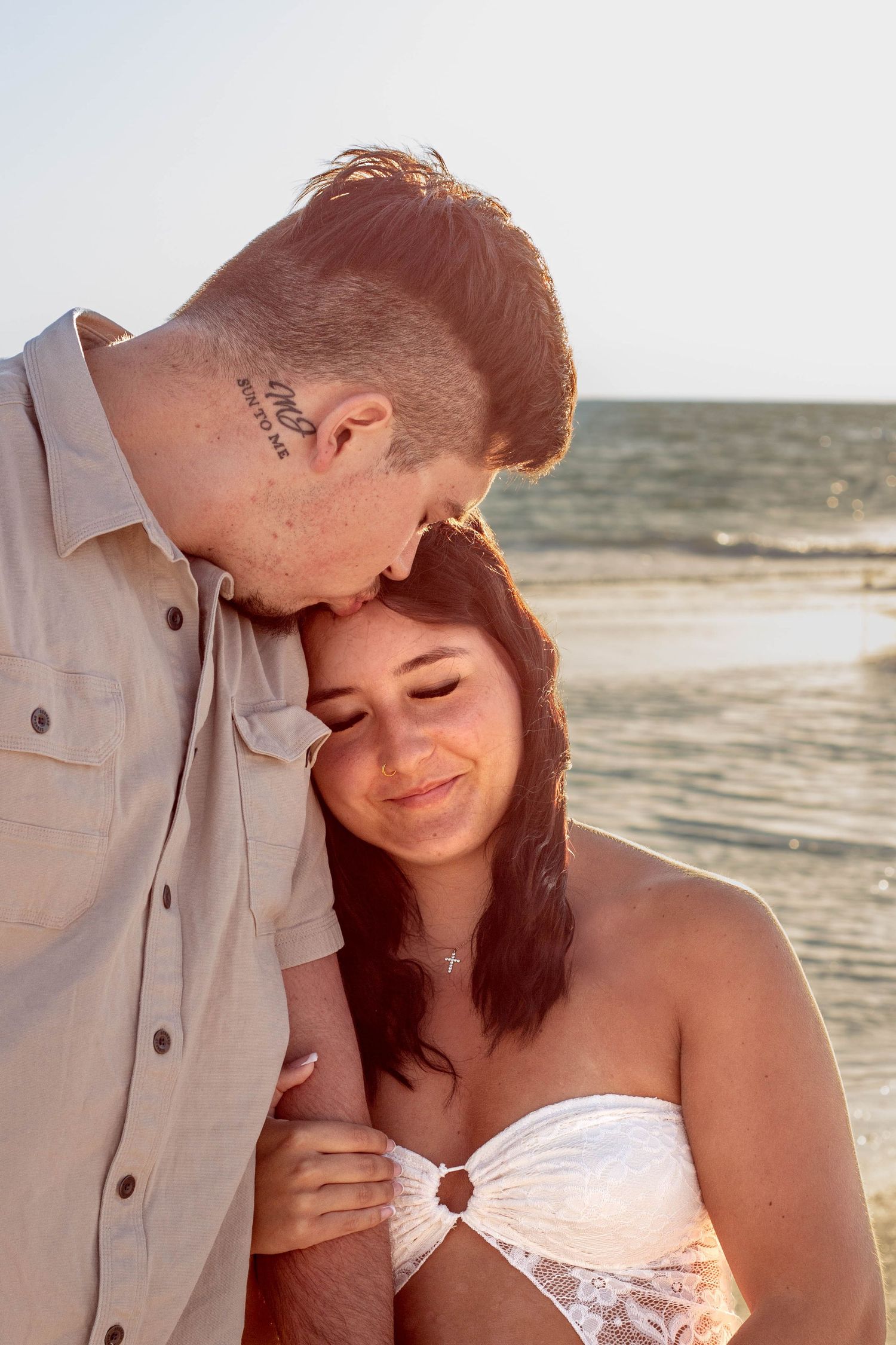 Couple sharing tender moment on beach, man kissing woman's forehead at golden hour.