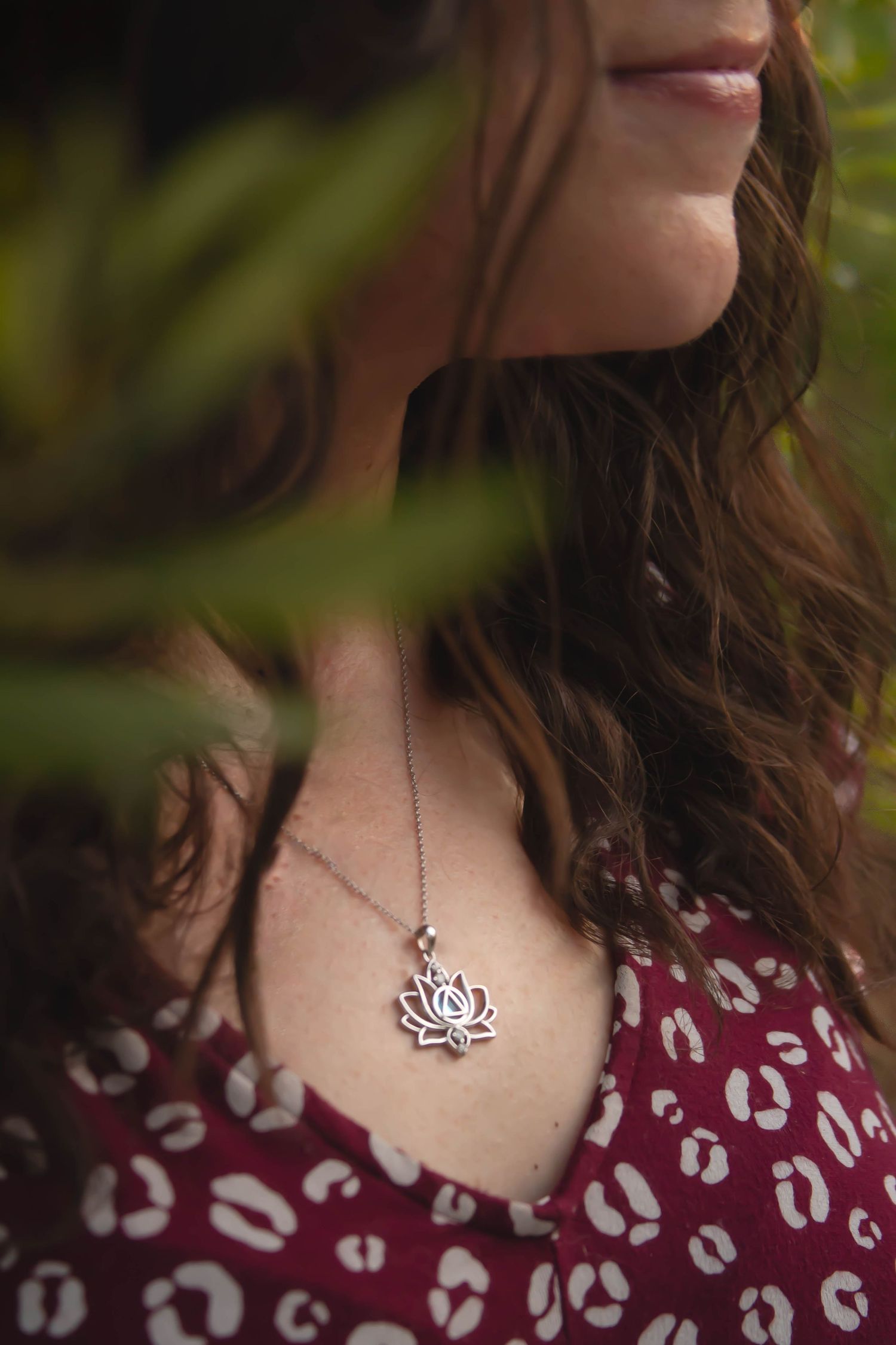 Close-up of a woman wearing a silver lotus flower pendant necklace with a burgundy patterned top.
