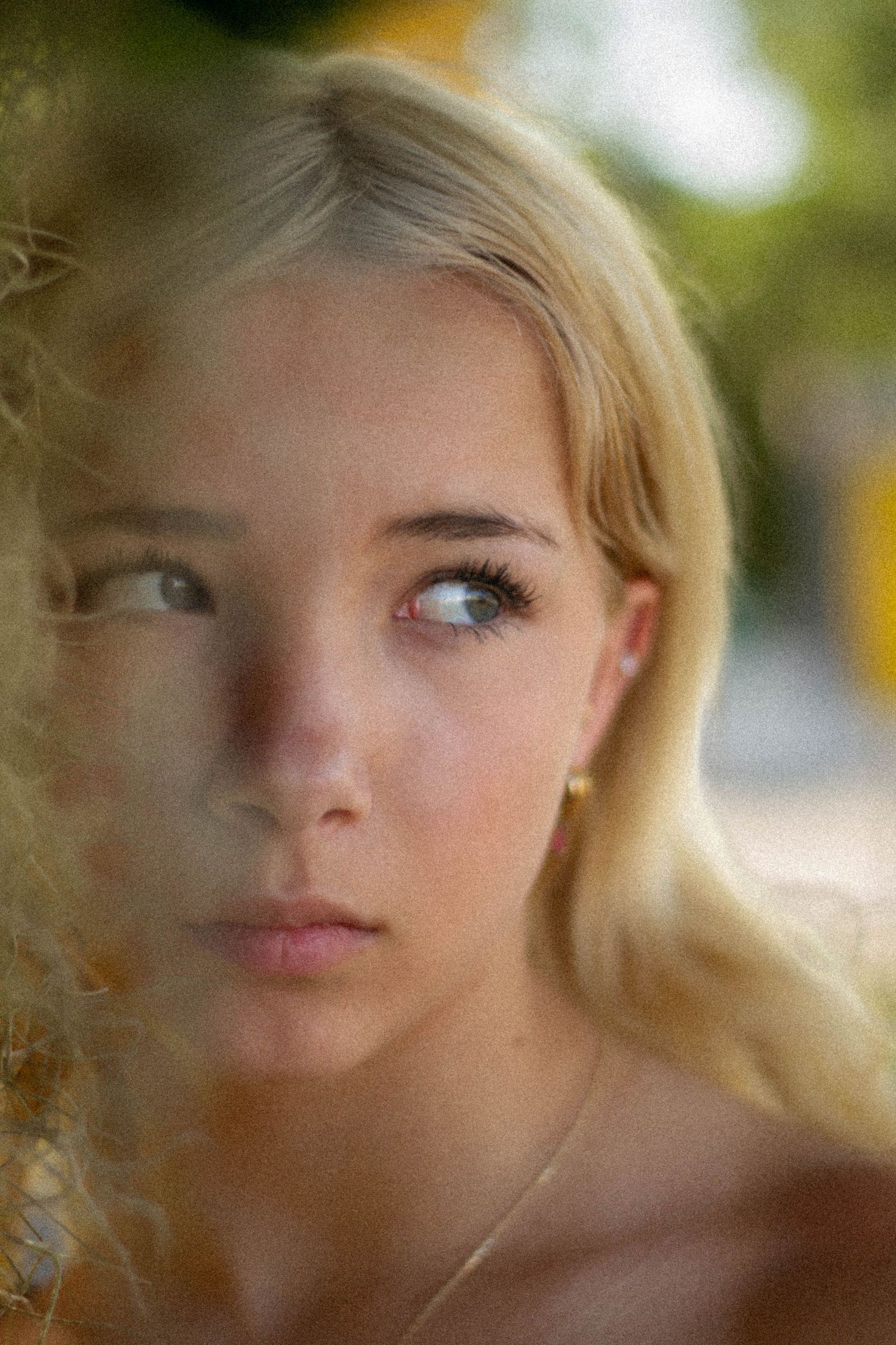 Close-up portrait of a young blonde woman with blue eyes wearing a delicate gold earring.