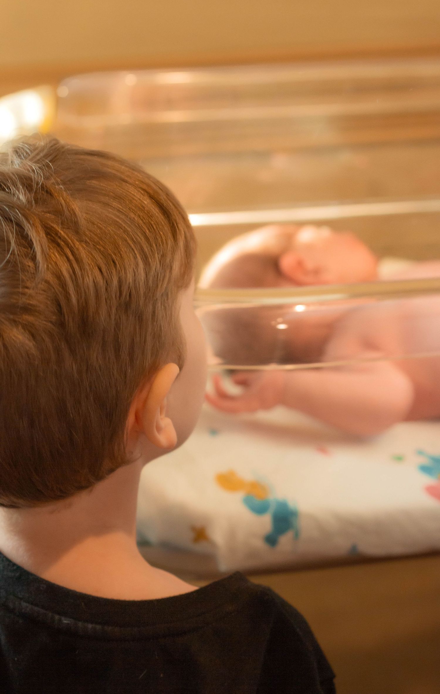 Young boy gazing at newborn baby lying in hospital bassinet, sibling meeting for the first time.