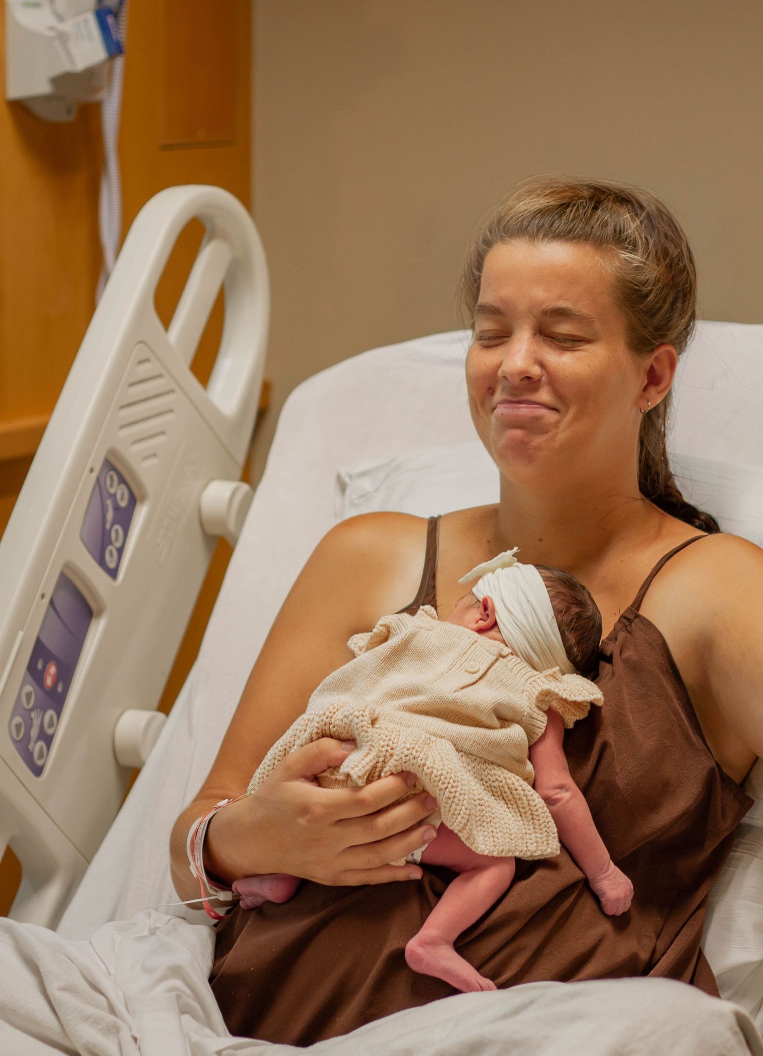 New mother smiling with eyes closed, cradling her newborn baby in a hospital bed after giving birth.