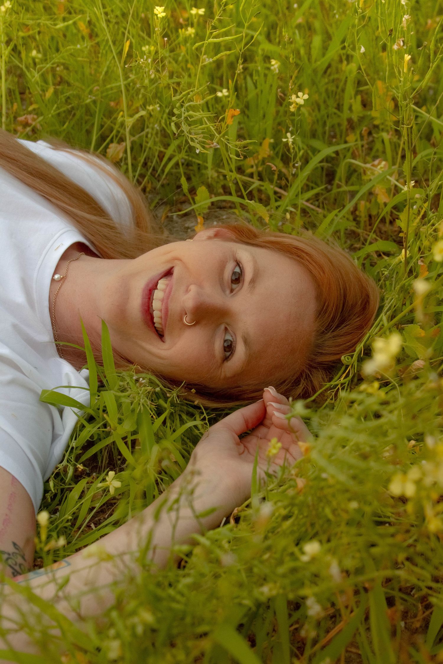 Smiling redhead woman lying in lush green meadow with wildflowers.