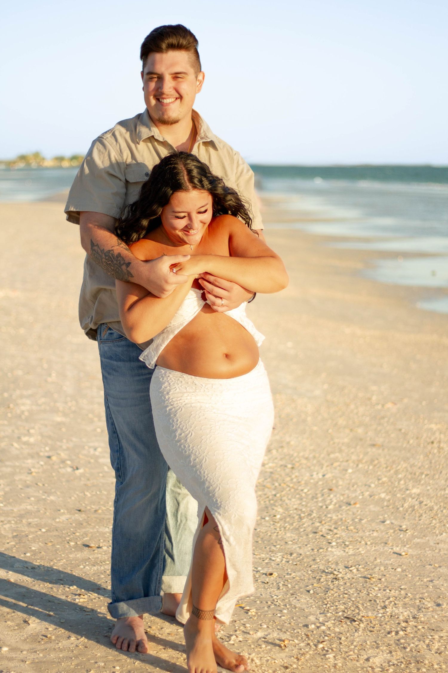 Happy couple embracing on sandy beach at golden hour sunset.