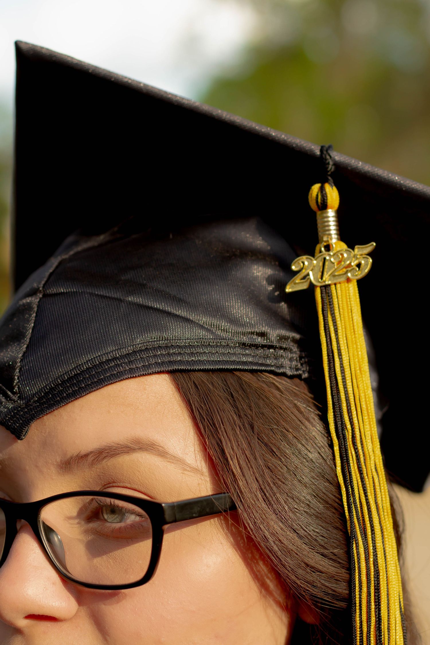 Close-up of graduation cap with gold 2025 tassel charm worn by student with glasses.