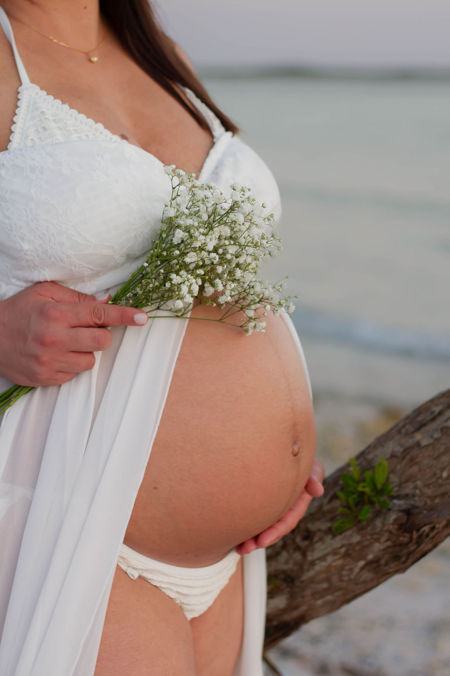 Close-up of pregnant belly with white wildflowers at beach.